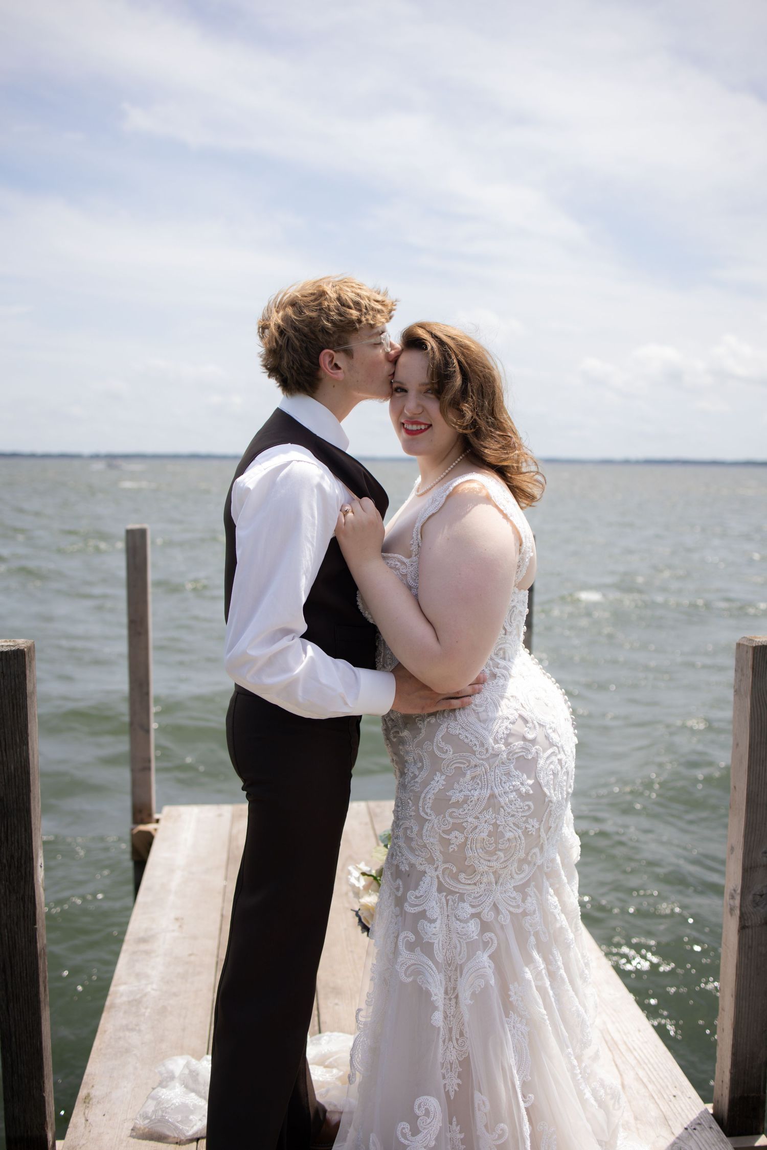 A romantic wedding couple embraces on a wooden dock overlooking a serene waterfront on their special day.