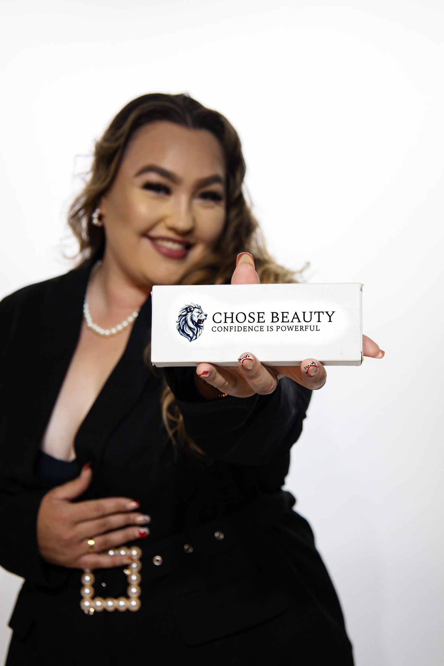 Professional showing white Chose Beauty branded product box against white background while wearing elegant black attire.
