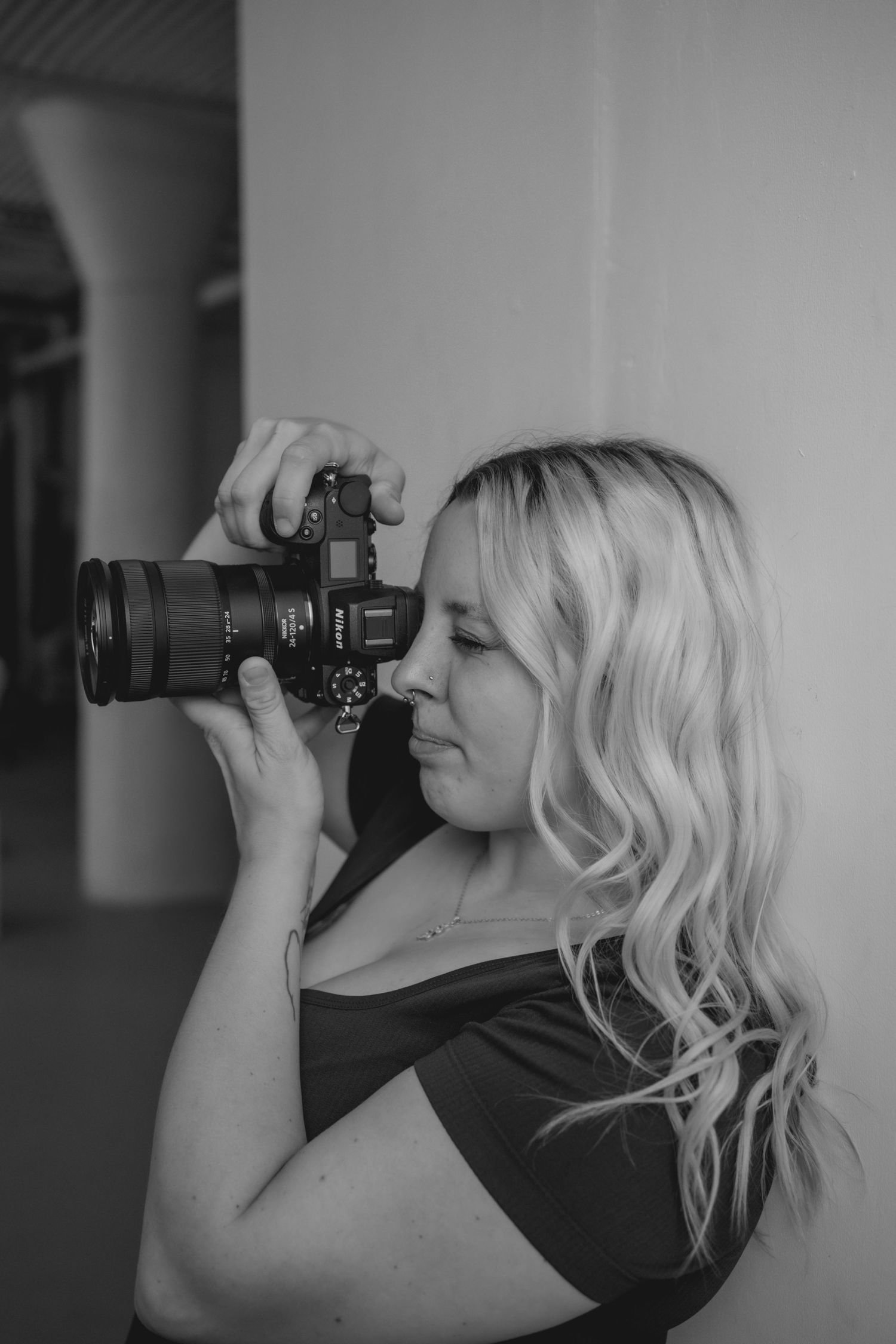A photographer in black clothing takes photos with a telephoto lens against a gray background in a series of similar poses.