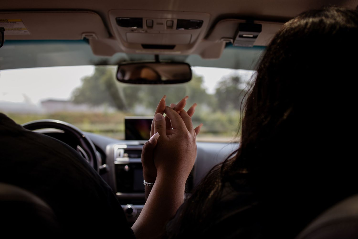 Person holding a phone while sitting in driver's seat of car, appearing to be using navigation while driving.