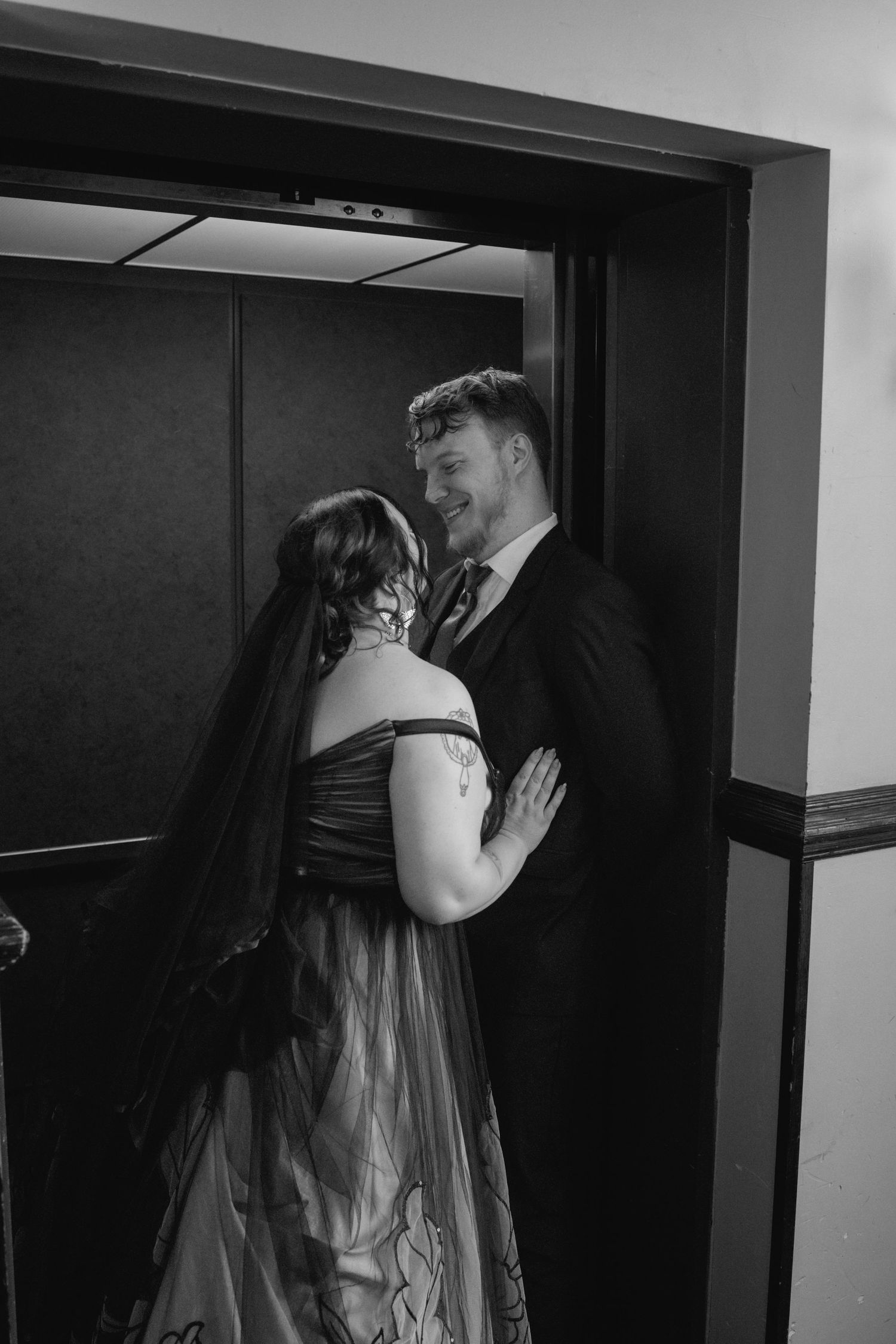 A romantic couple in formal attire share an intimate moment in an elevator, with the woman wearing a black gown.