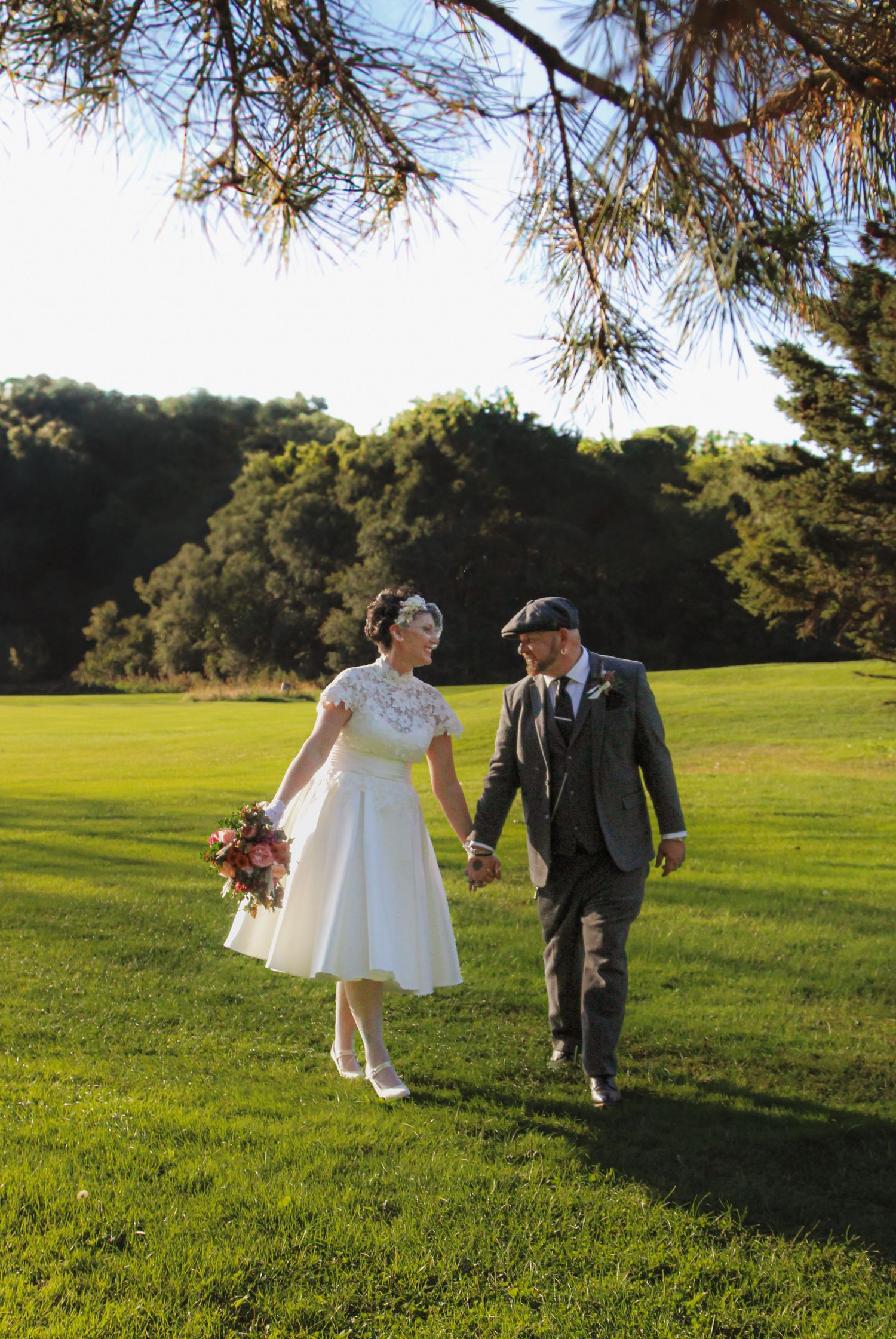 Two figures walk hand-in-hand through a sun-dappled green meadow on a beautiful autumn day.