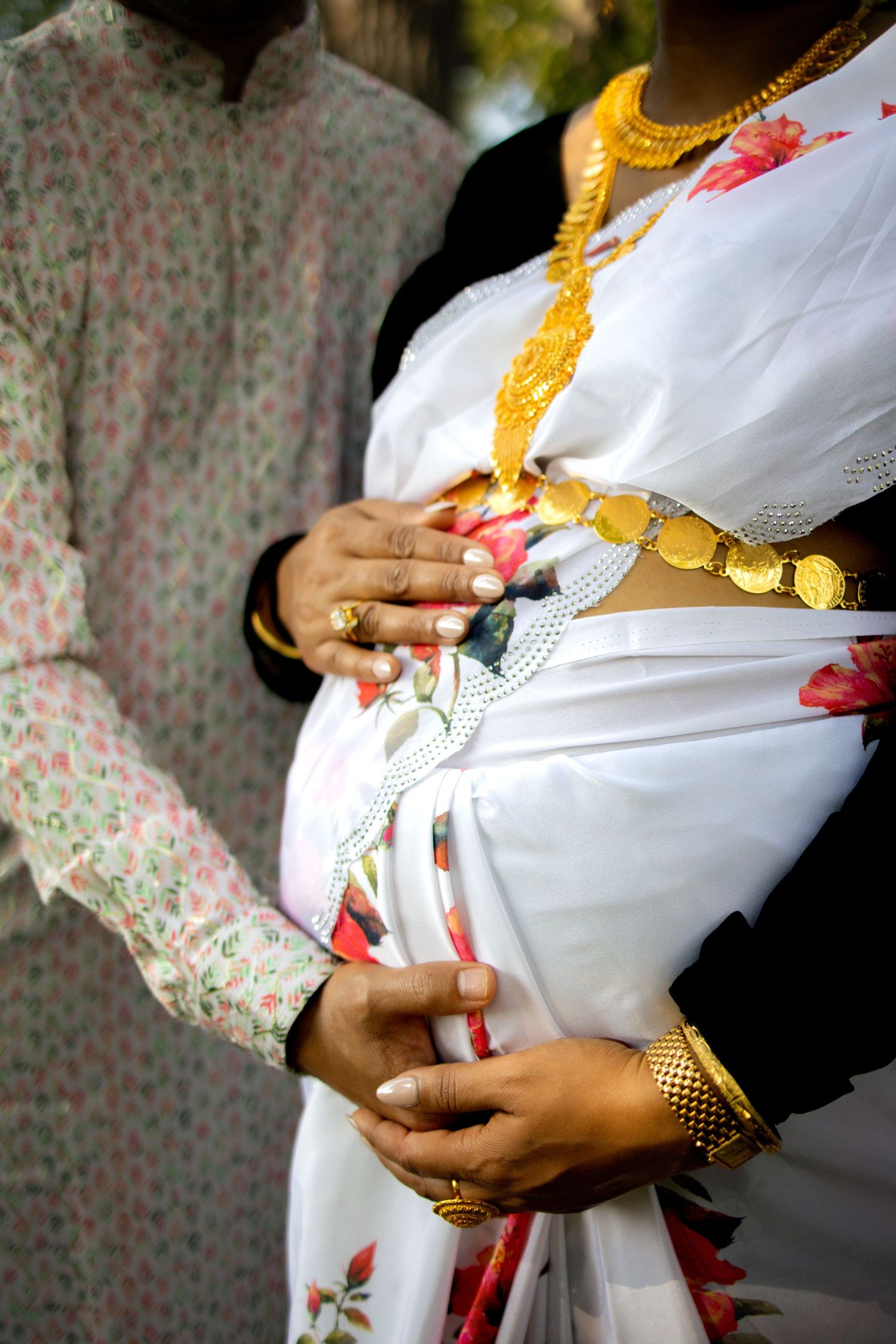 Close up view of traditional Indian wedding attire showing white floral sari, gold necklace and rings on hands.