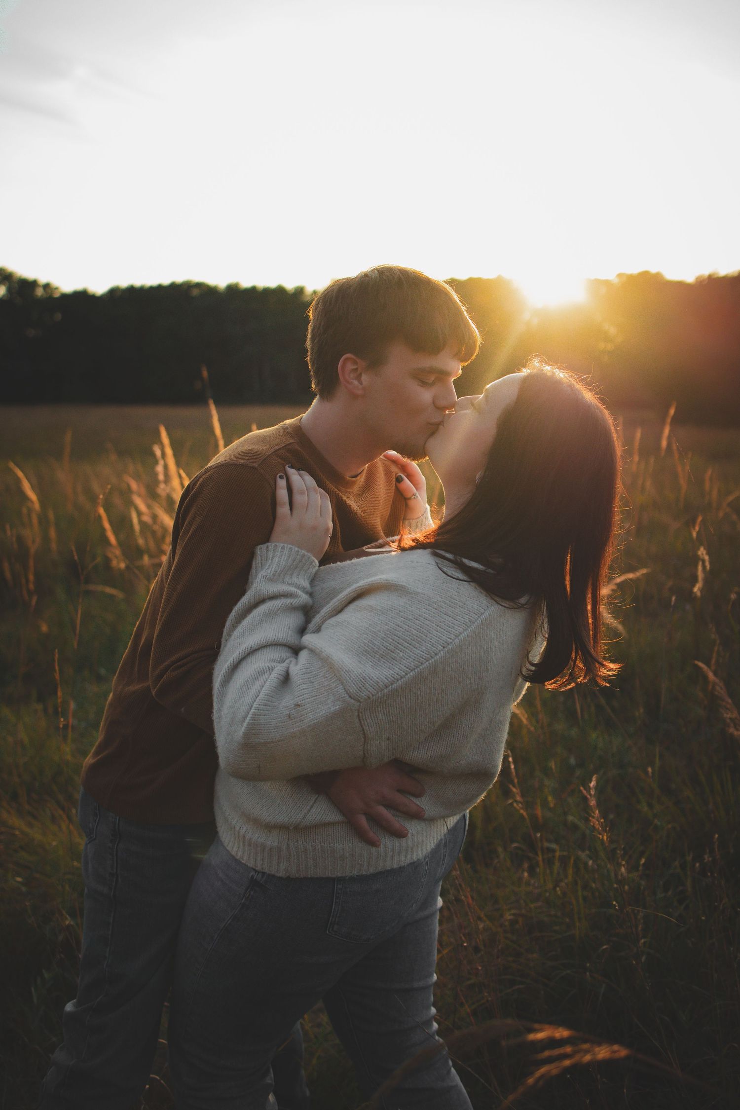 Romantic couple embraces in golden sunset light among tall grass in a summer field.