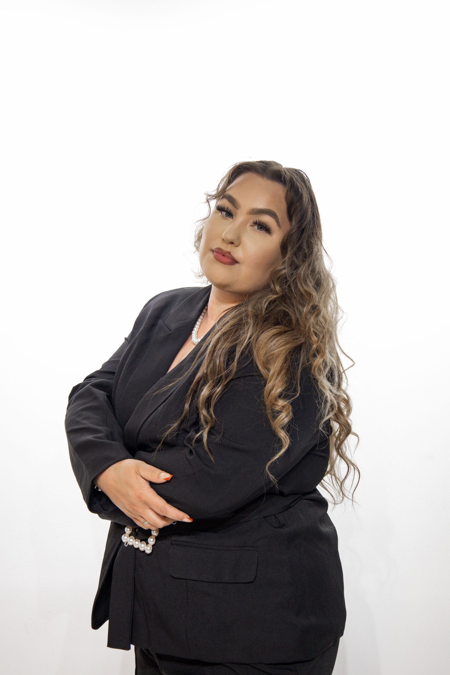 Professional portrait against white background showing confident pose in black business suit with wavy hair.