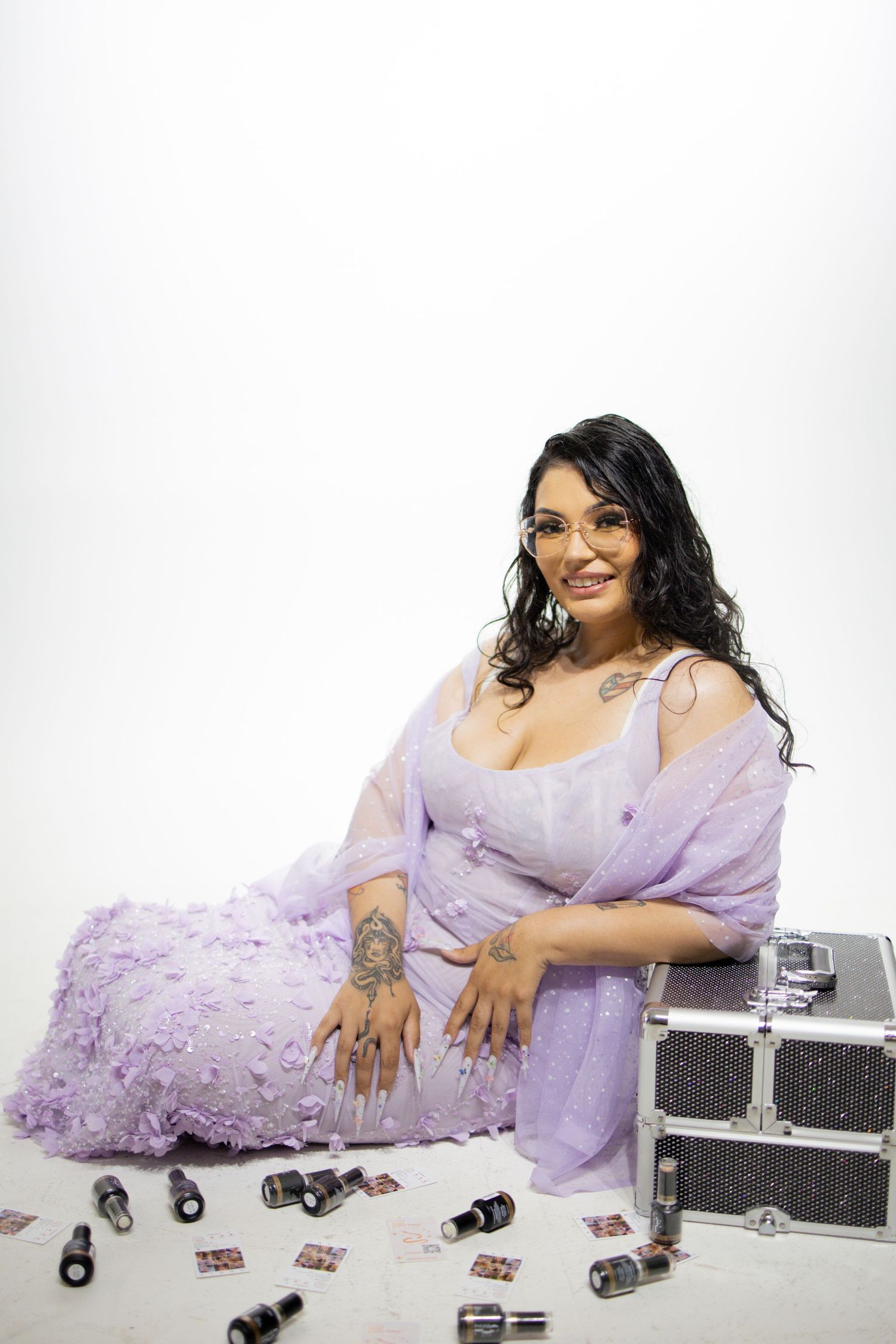Someone in a flowing lavender dress poses with tarot cards and jewelry boxes against a white backdrop.