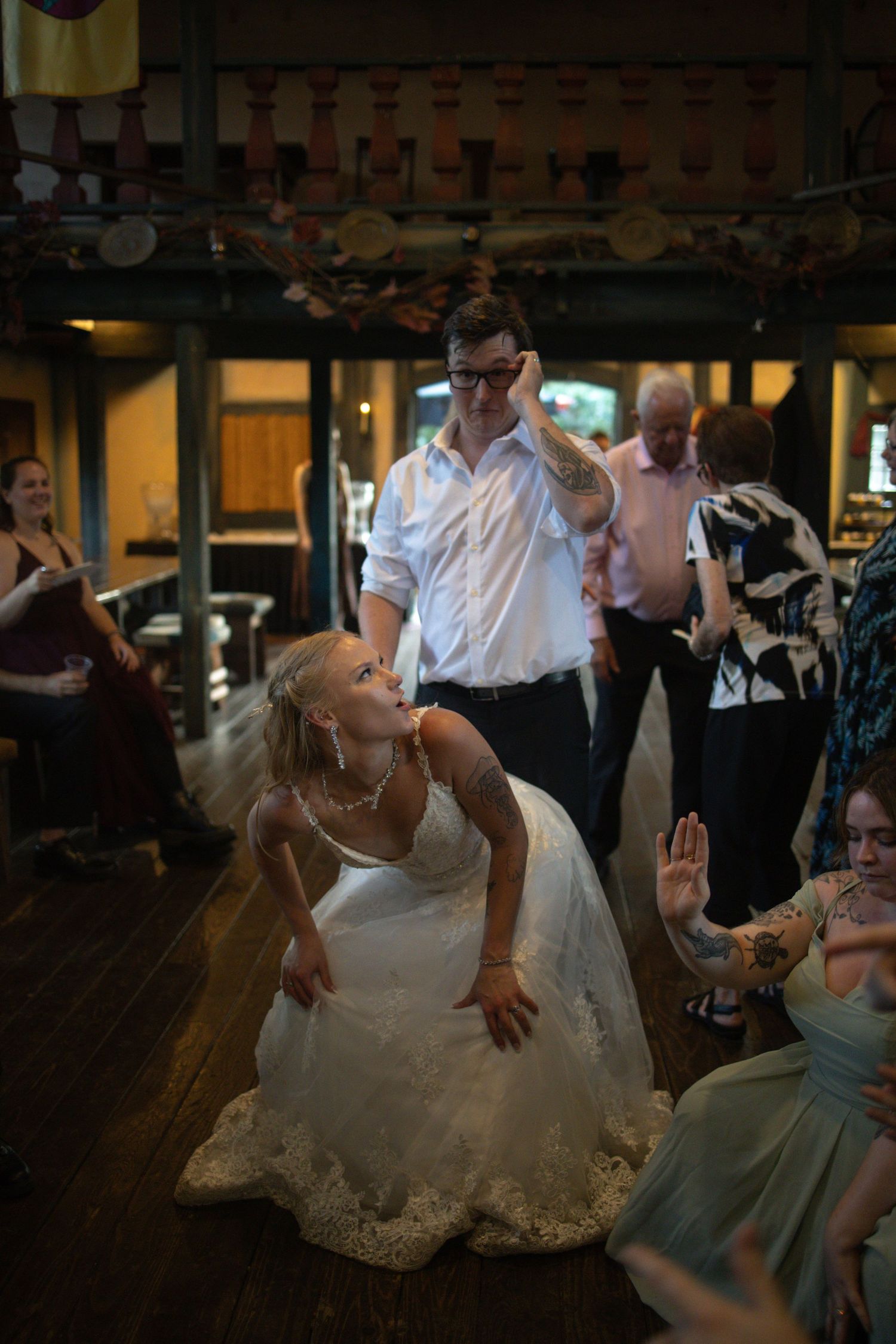 A couple dances energetically at their wedding reception on a dark wooden dance floor with guests in the background.
