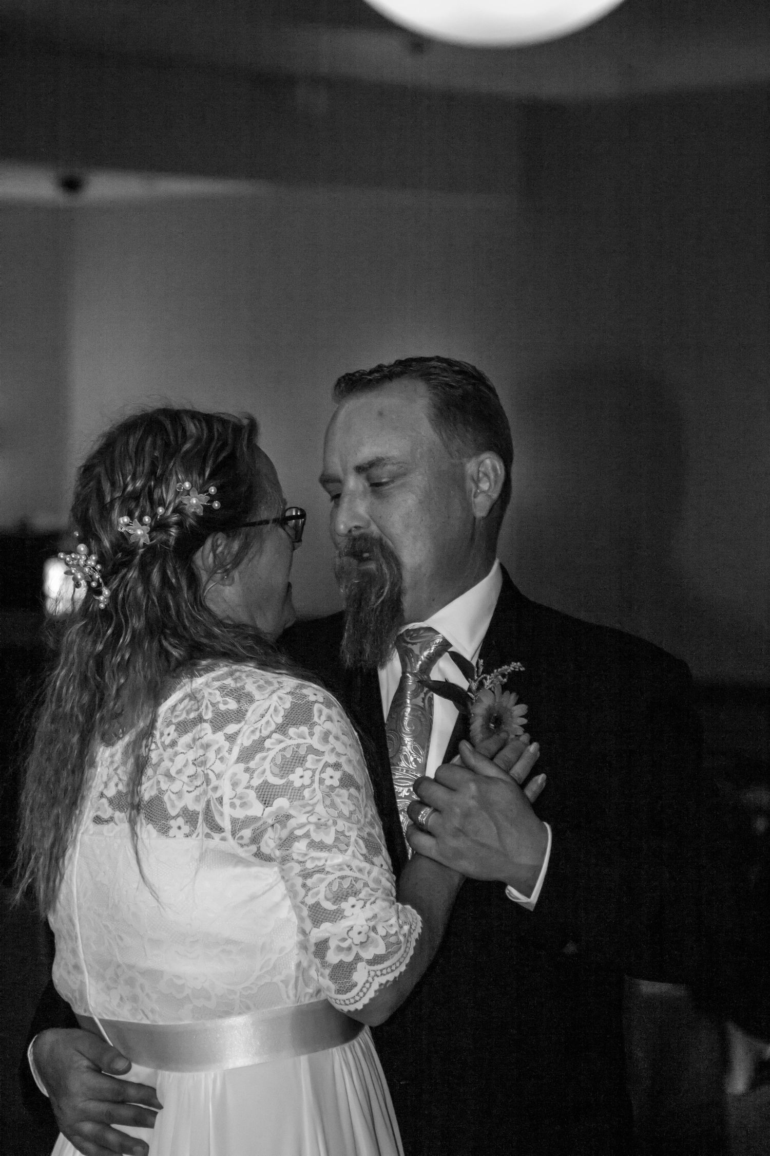 A couple shares an intimate dance moment in black and white, with the woman wearing a lace dress and floral crown.