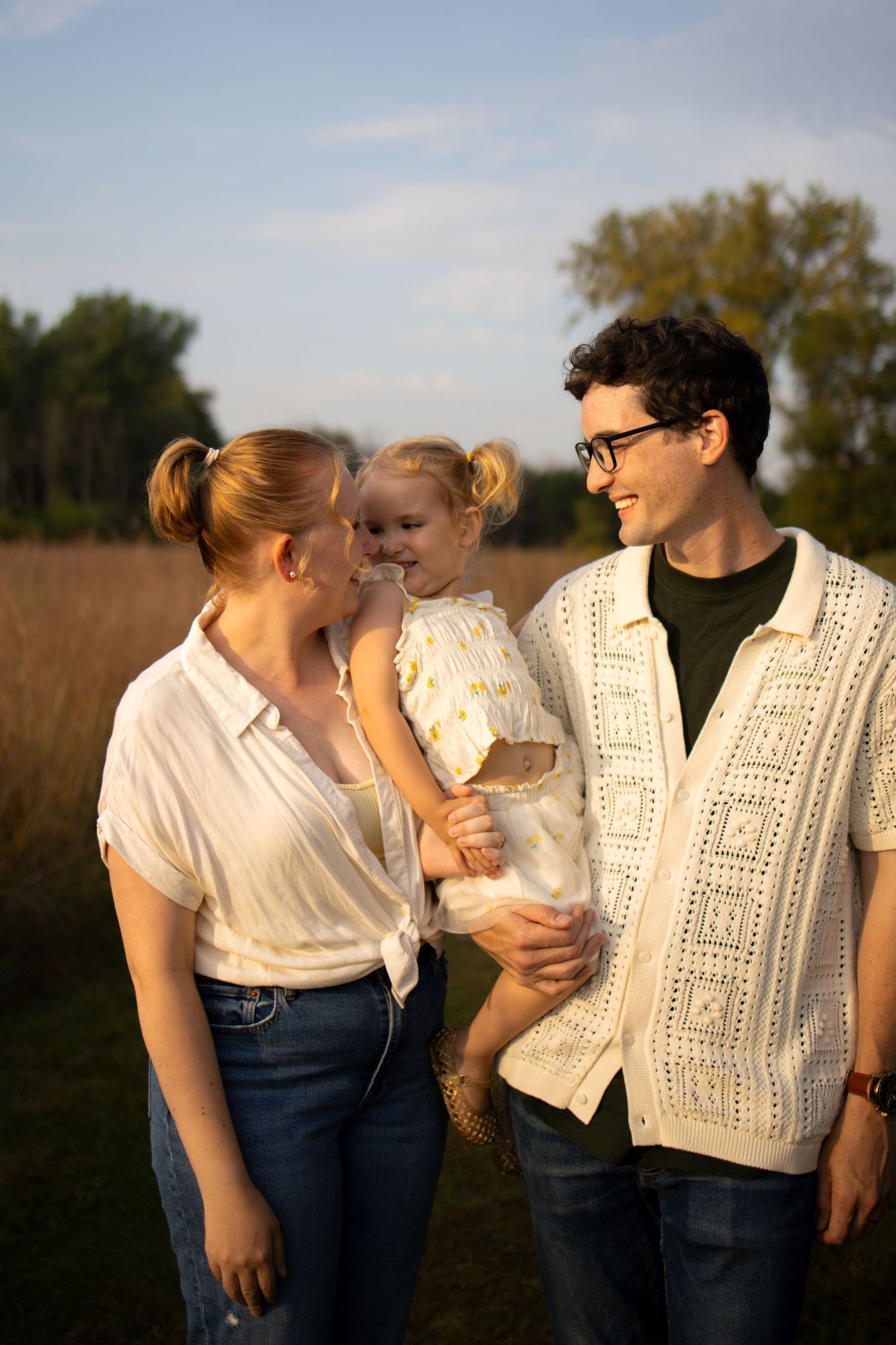 A family wearing white and denim embraces outdoors during golden hour.