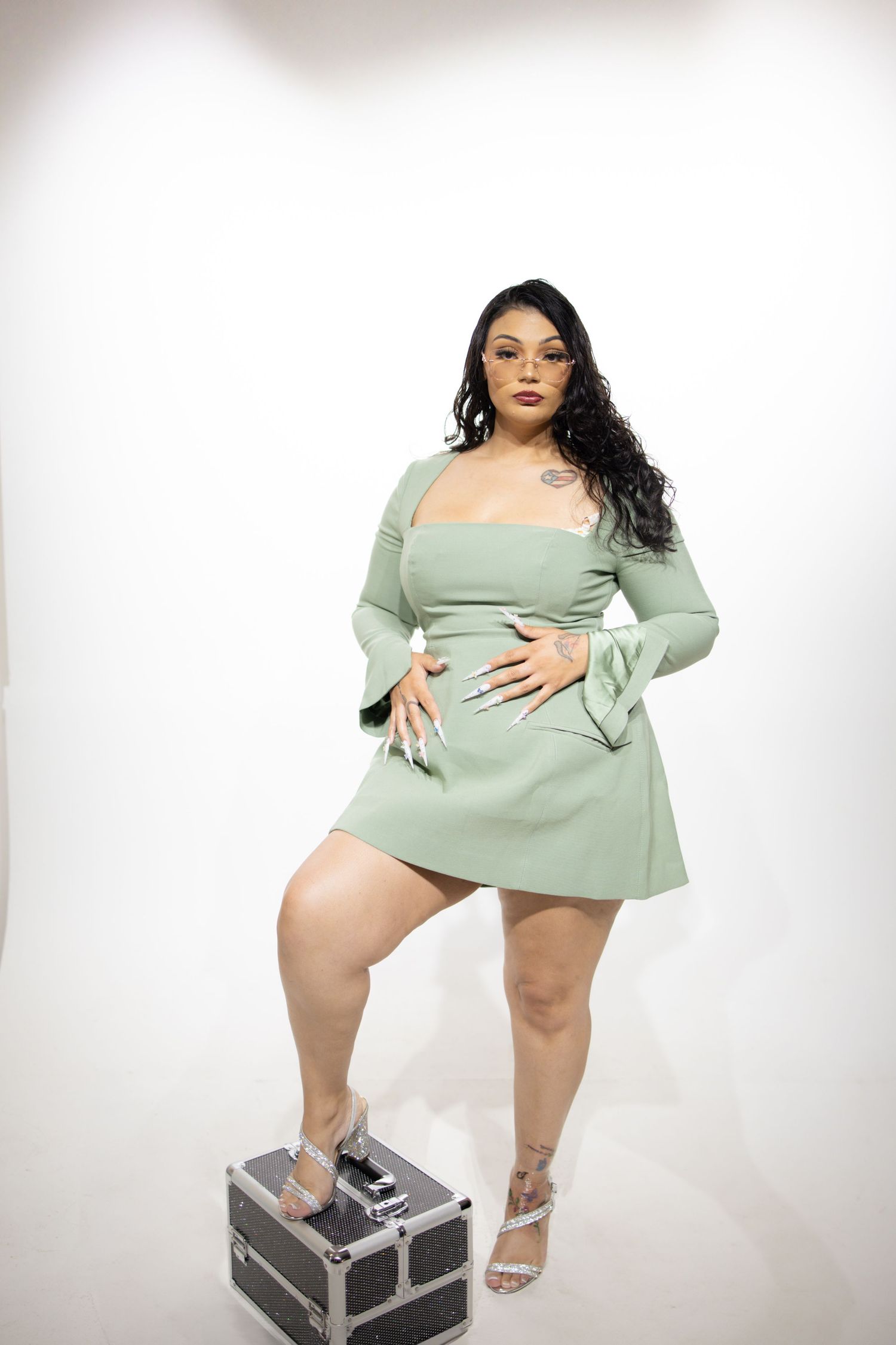 A model wearing a mint green mini dress with flared sleeves poses confidently on a storage case against a white background.