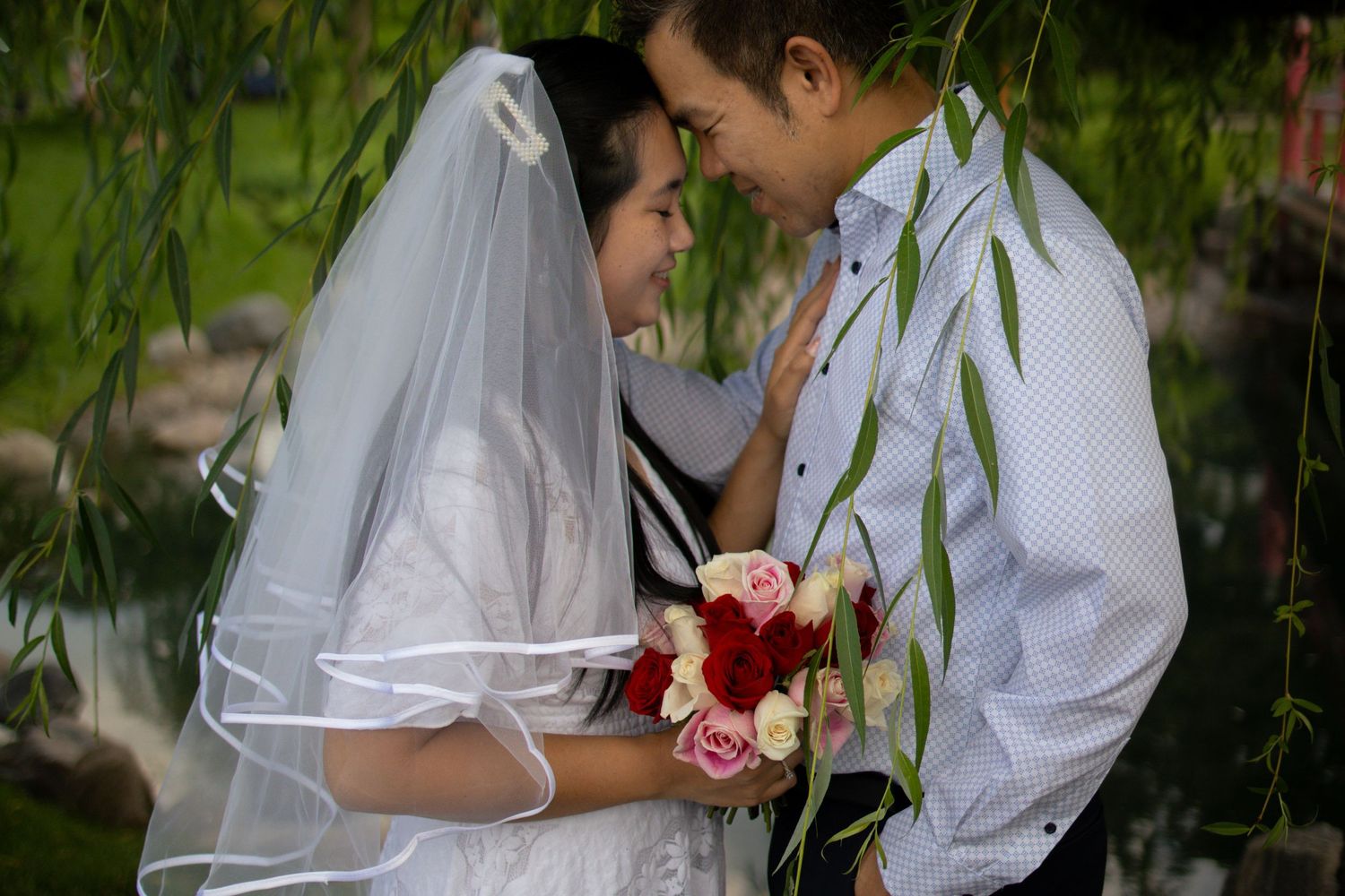 A tender intimate moment between newlyweds beneath drooping willow branches with bridal flowers.