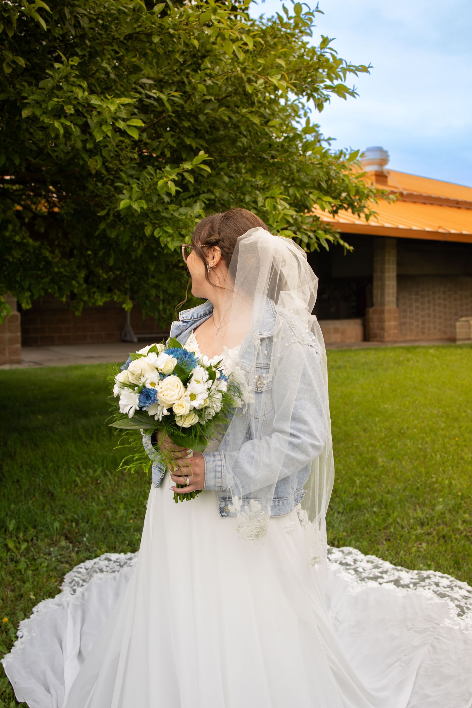 A person in an elegant white wedding dress sits gracefully on green grass with their flowing dress spread around them.