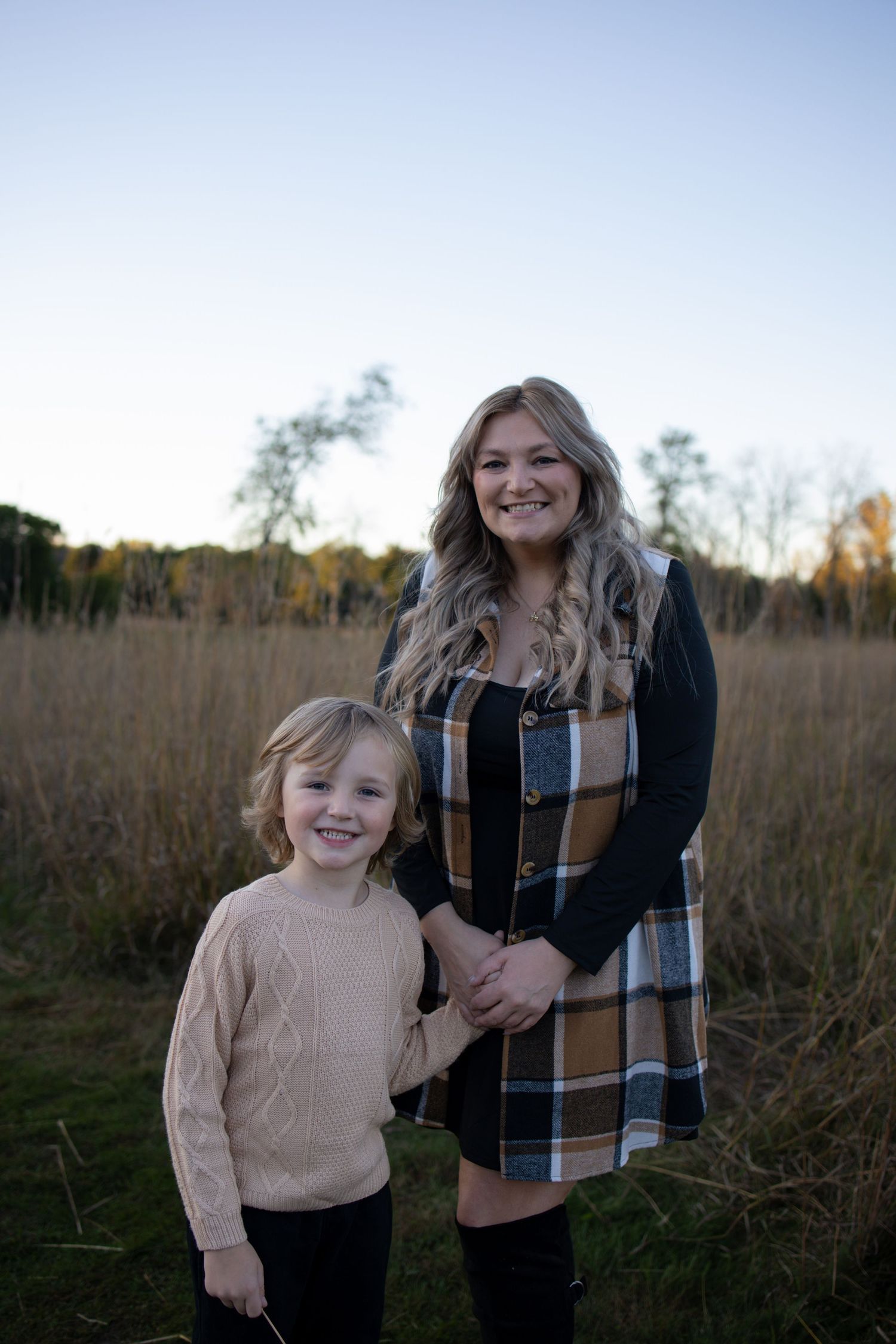 A parent and child hold hands while standing together in a golden autumn field at sunset.