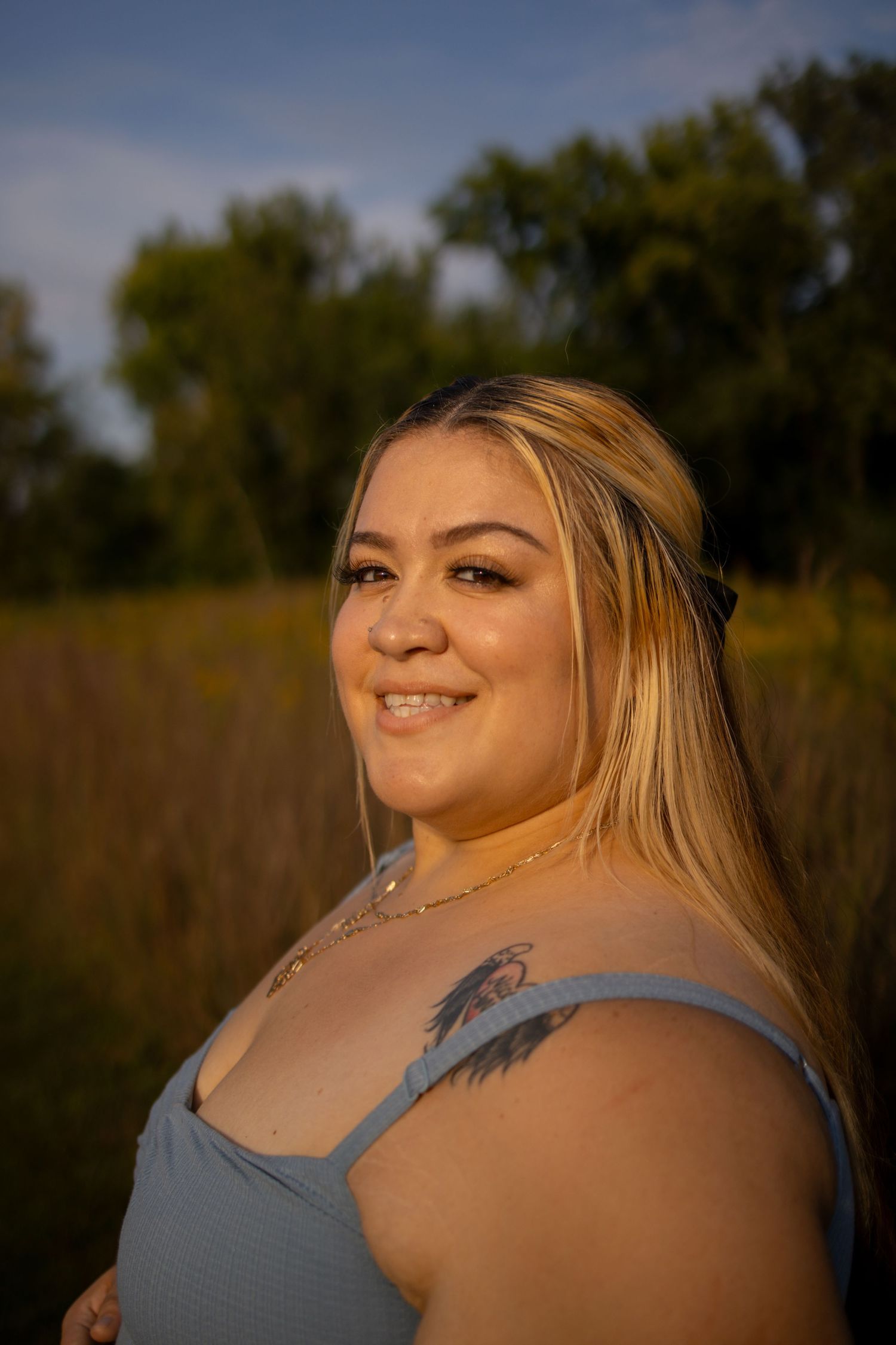 Portrait of someone with blonde hair wearing a blue tank top in golden sunlight against a natural outdoor background.