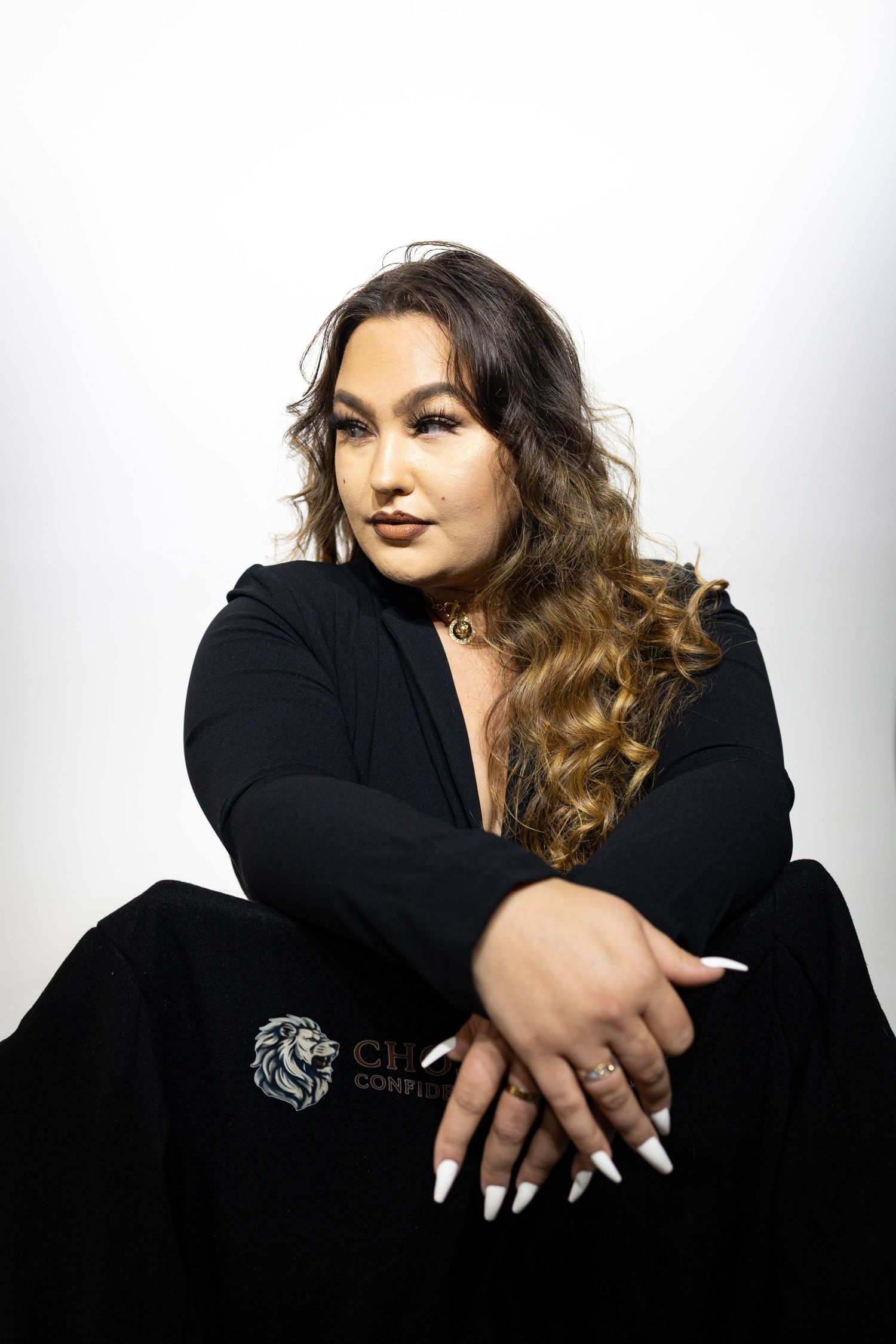 Professional portrait of a model in a black outfit posing confidently against a white background.