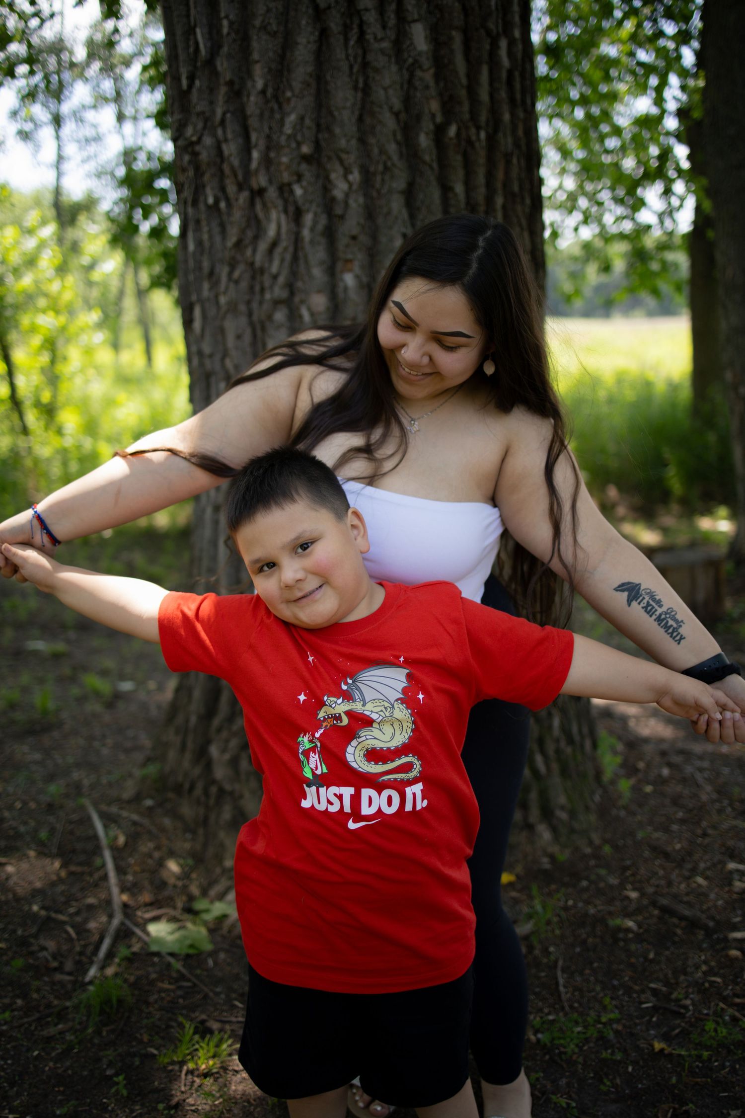 A playful moment captured under a large tree trunk, with a red t-shirt featuring a dinosaur Just Do It design.