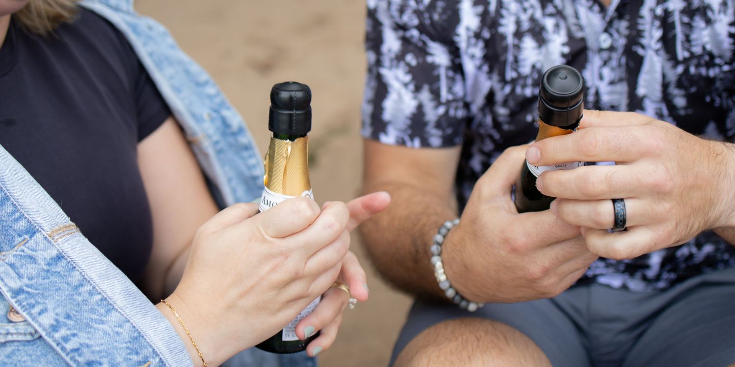 Hands holding wine and champagne bottles in a casual social gathering or party setting.