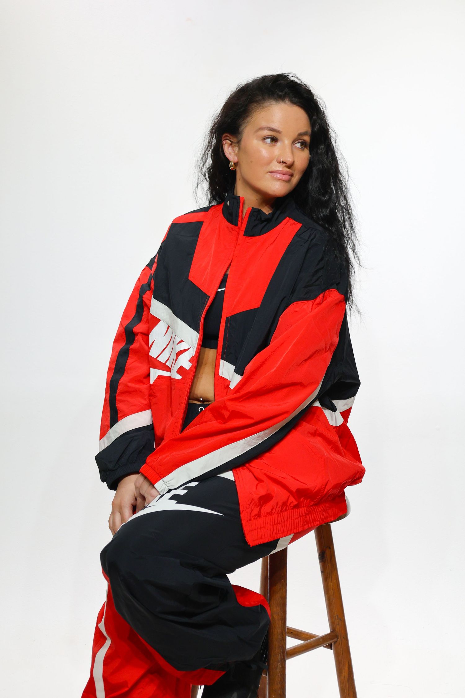 Athletic apparel fashion photo series showing red and black Nike windbreaker sportswear on wooden stool against white backdrop.
