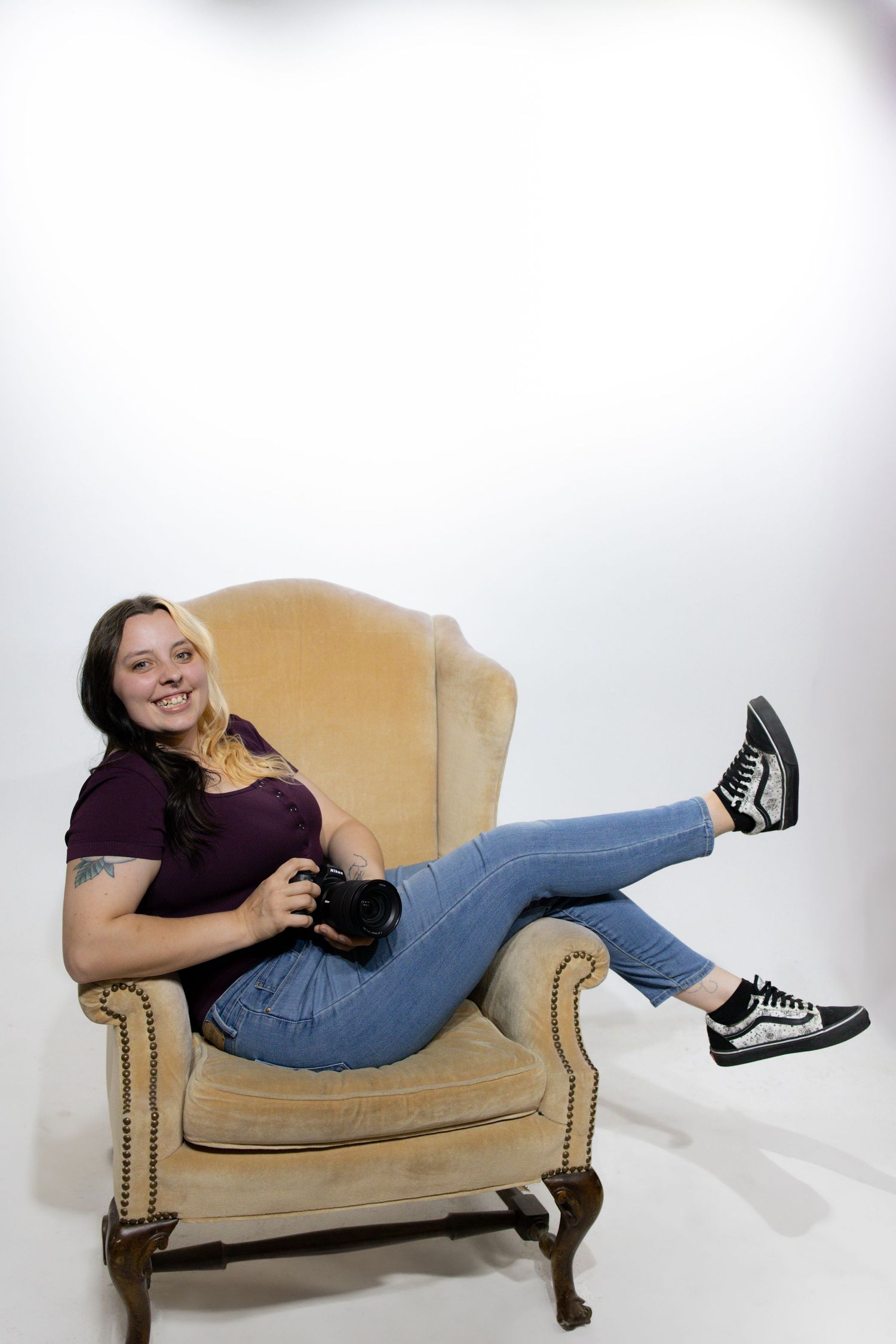 Someone lounges casually in a beige vintage armchair wearing jeans, a purple shirt and sneakers.