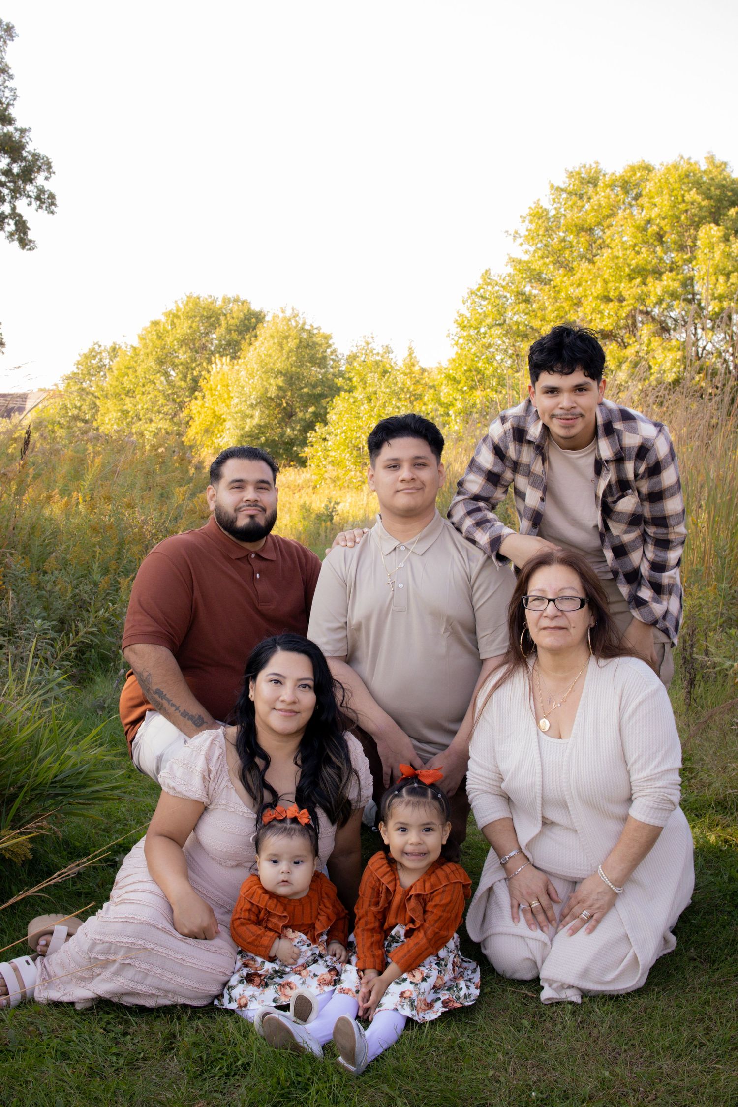 A family poses together outdoors against autumn trees with golden foliage in the background.