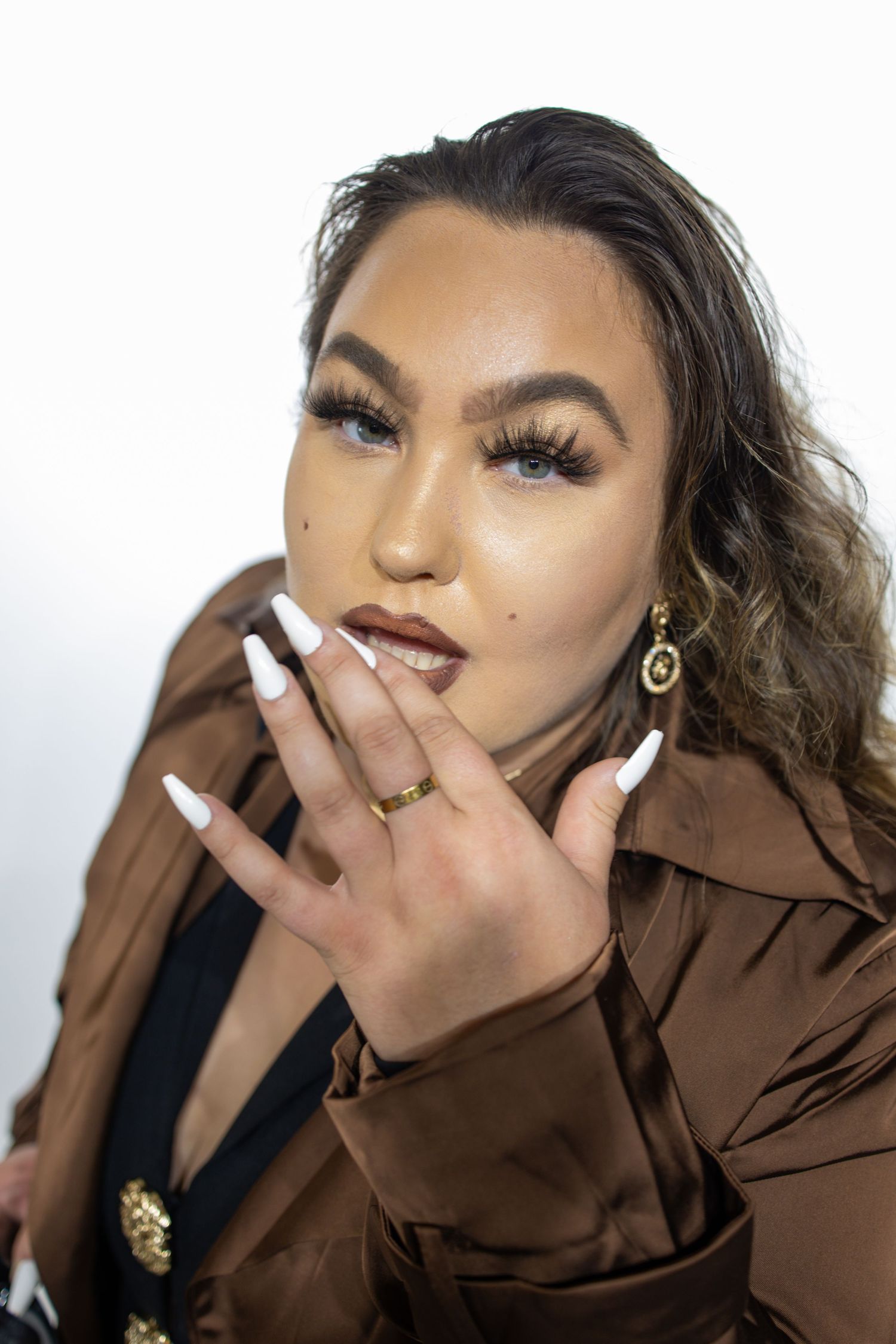 A person in brown attire poses for a series of expressive selfies with dramatic makeup and jewelry.