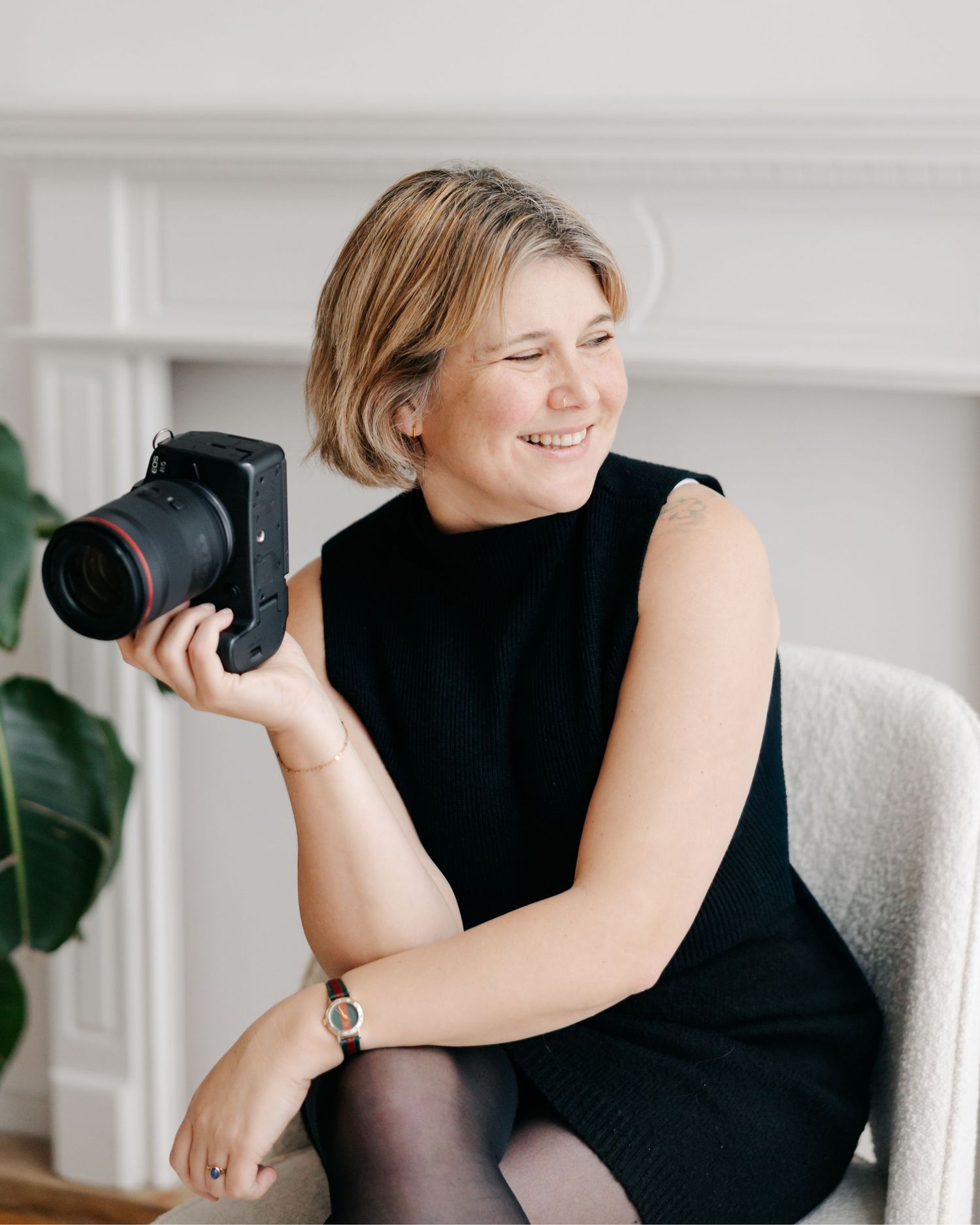 A person in a black sleeveless top takes photos with a camera while sitting in a bright, modern interior space.