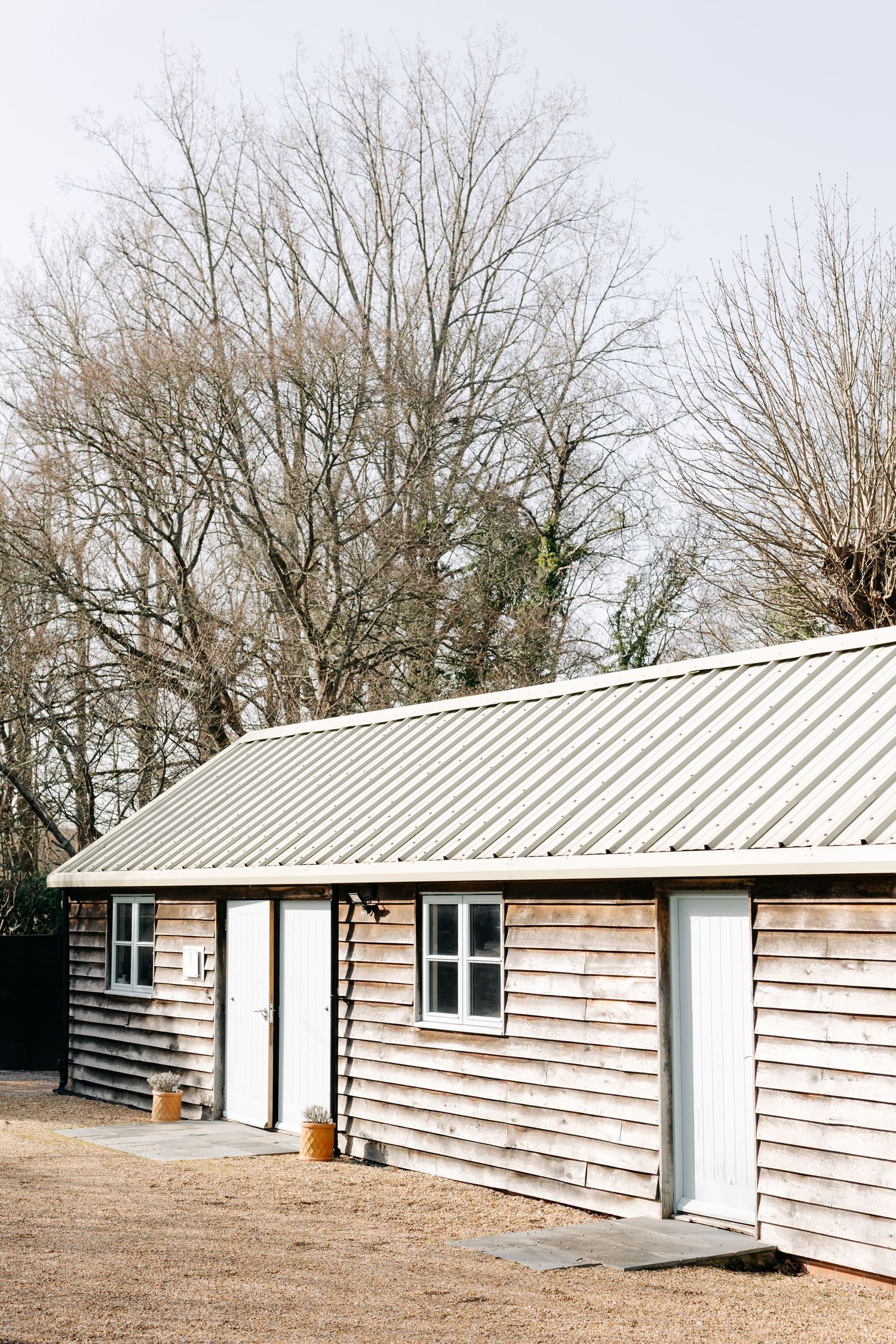 Rustic wooden cabin with corrugated metal roof surrounded by bare winter trees on a clear day.