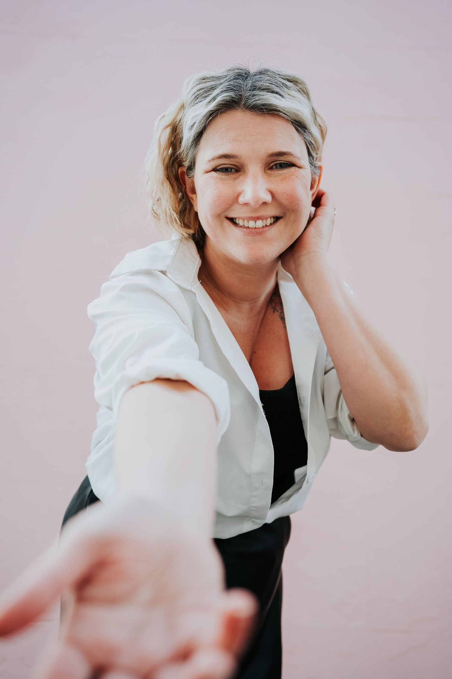 A selfie portrait in casual attire with a white button-down shirt against a pink background.