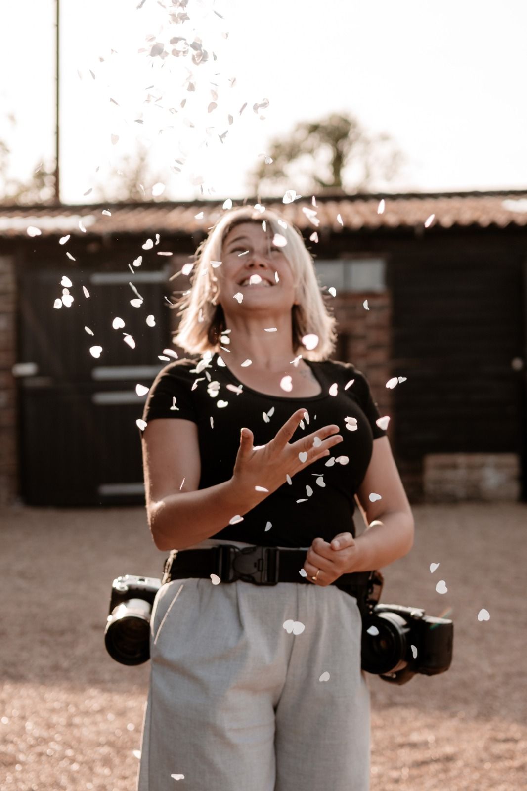 A joyful moment captured in sunlight as white petals float through the air around a person in a black shirt and gray pants.
