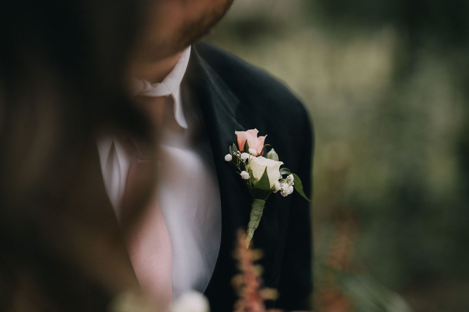 A delicate pink and white boutonniere pinned to a dark suit jacket lapel.