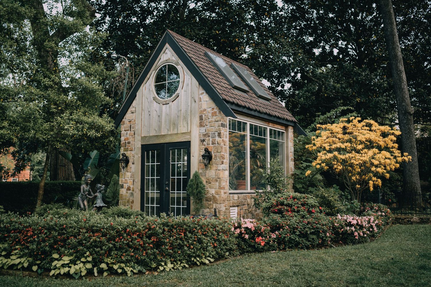 Charming cottage-style house exterior with stone facade and autumn foliage in the background.