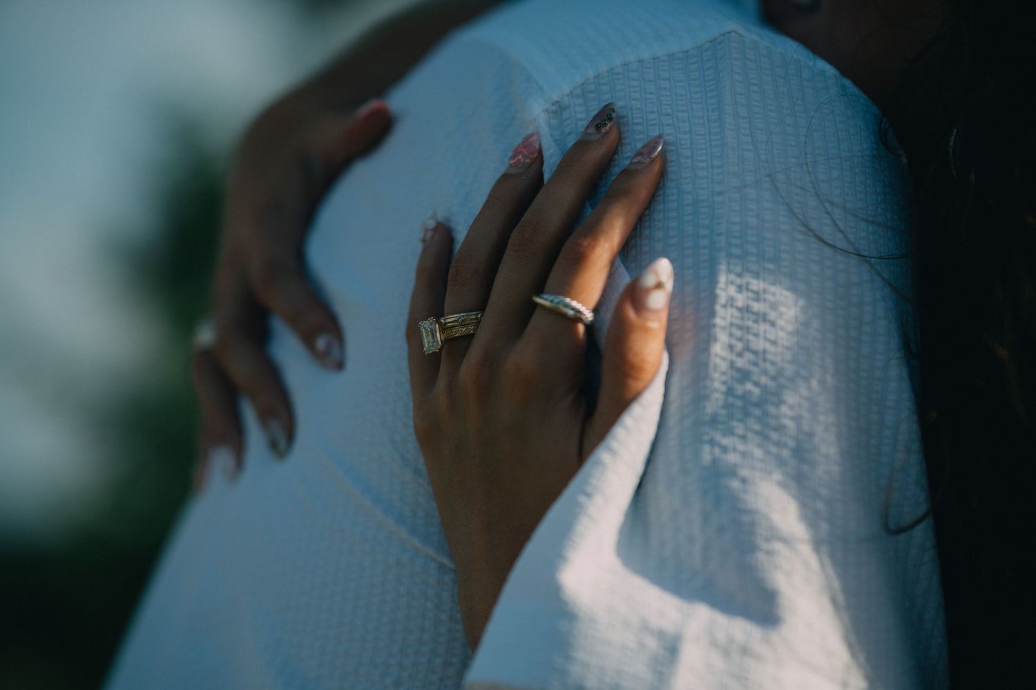 Close-up detail shot of hands touching white tulle fabric with an engagement ring.