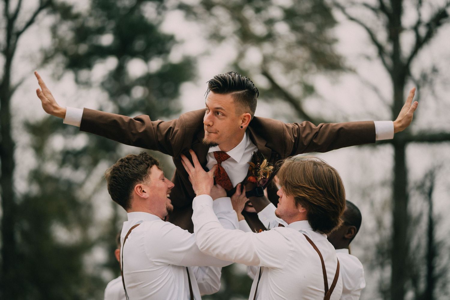 Groomsmen lift and support someone in a celebratory pose during a wedding.