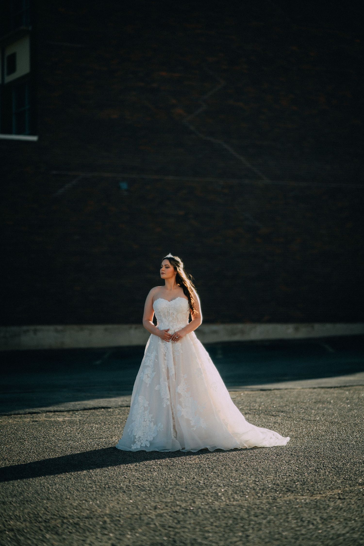 A bride in a flowing white ballgown poses on textured pavement during a dramatic sunset photoshoot.