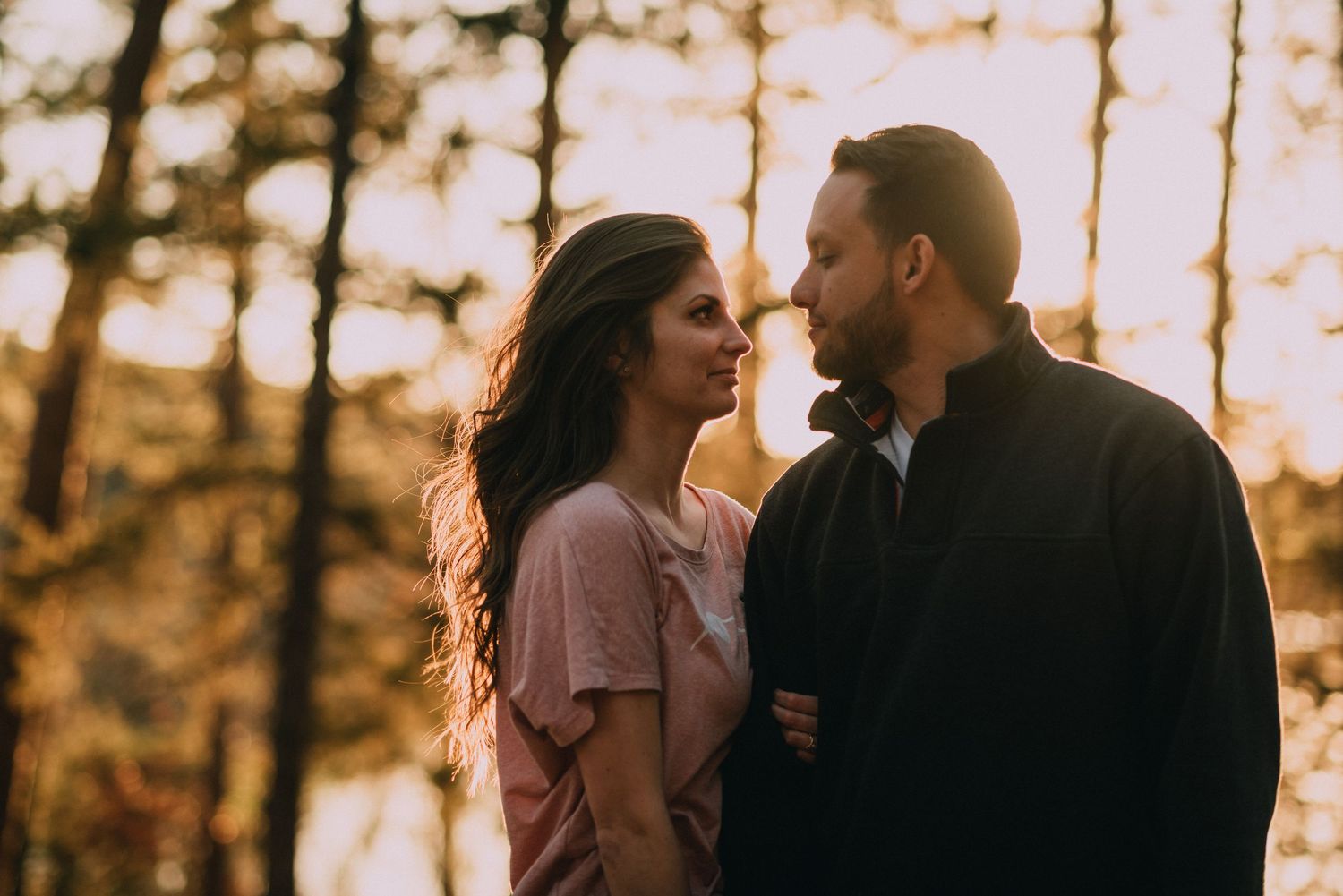 Intimate couple portrait silhouetted against sunset through trees.