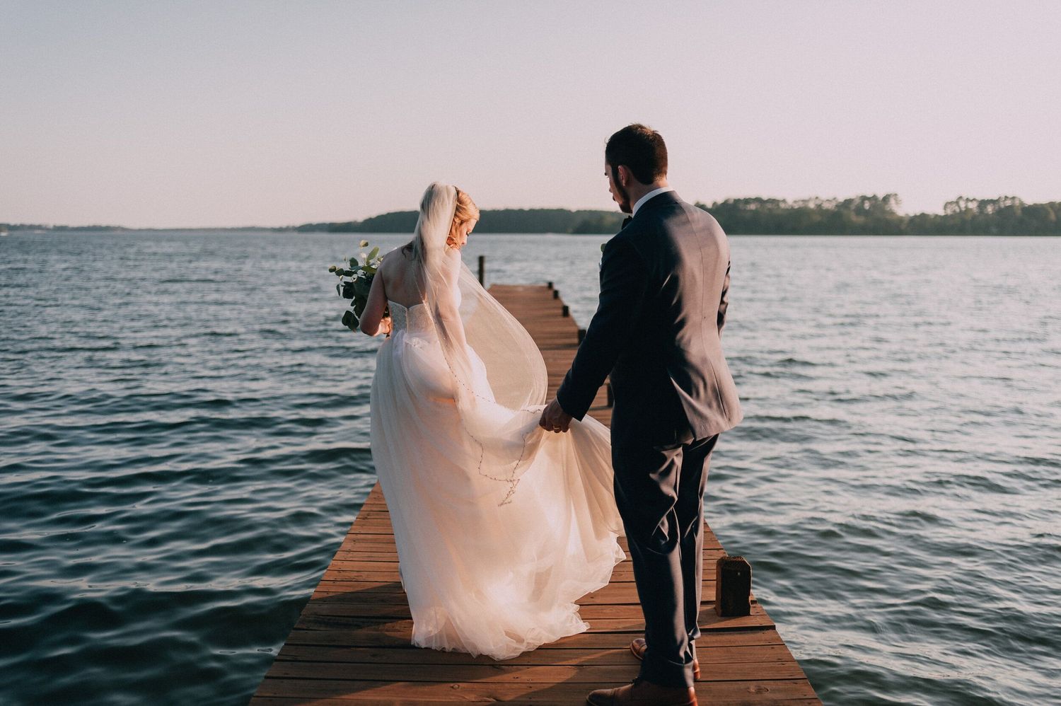 Couple walking on wooden dock by lake during sunset.