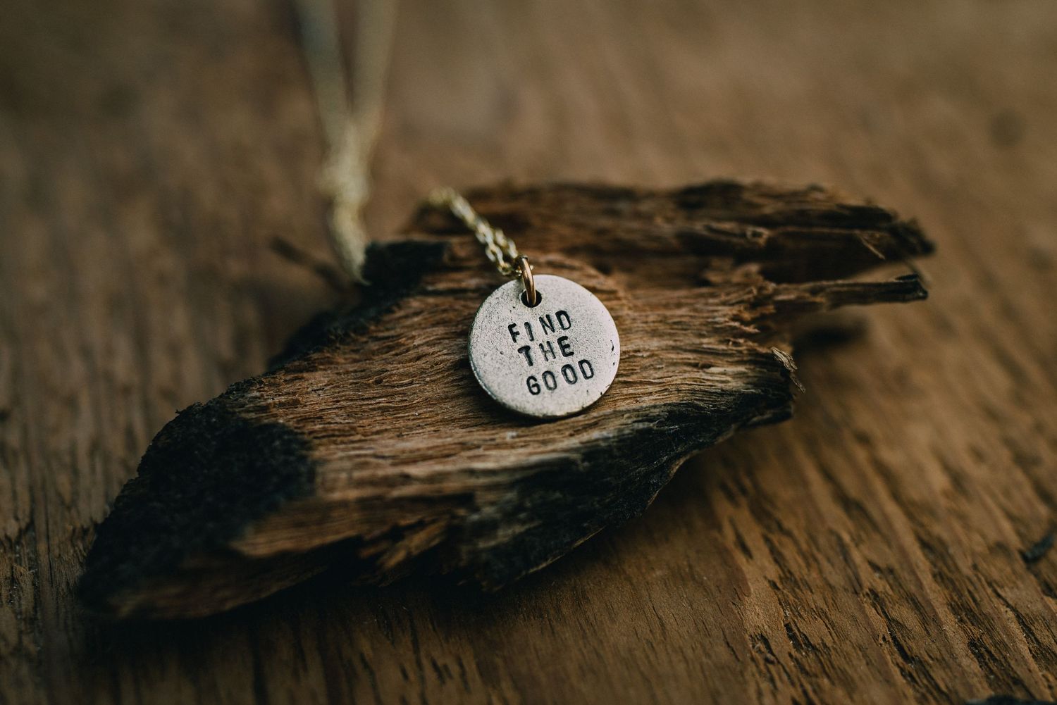 Close-up of a small metal heart charm with text resting on weathered wood.