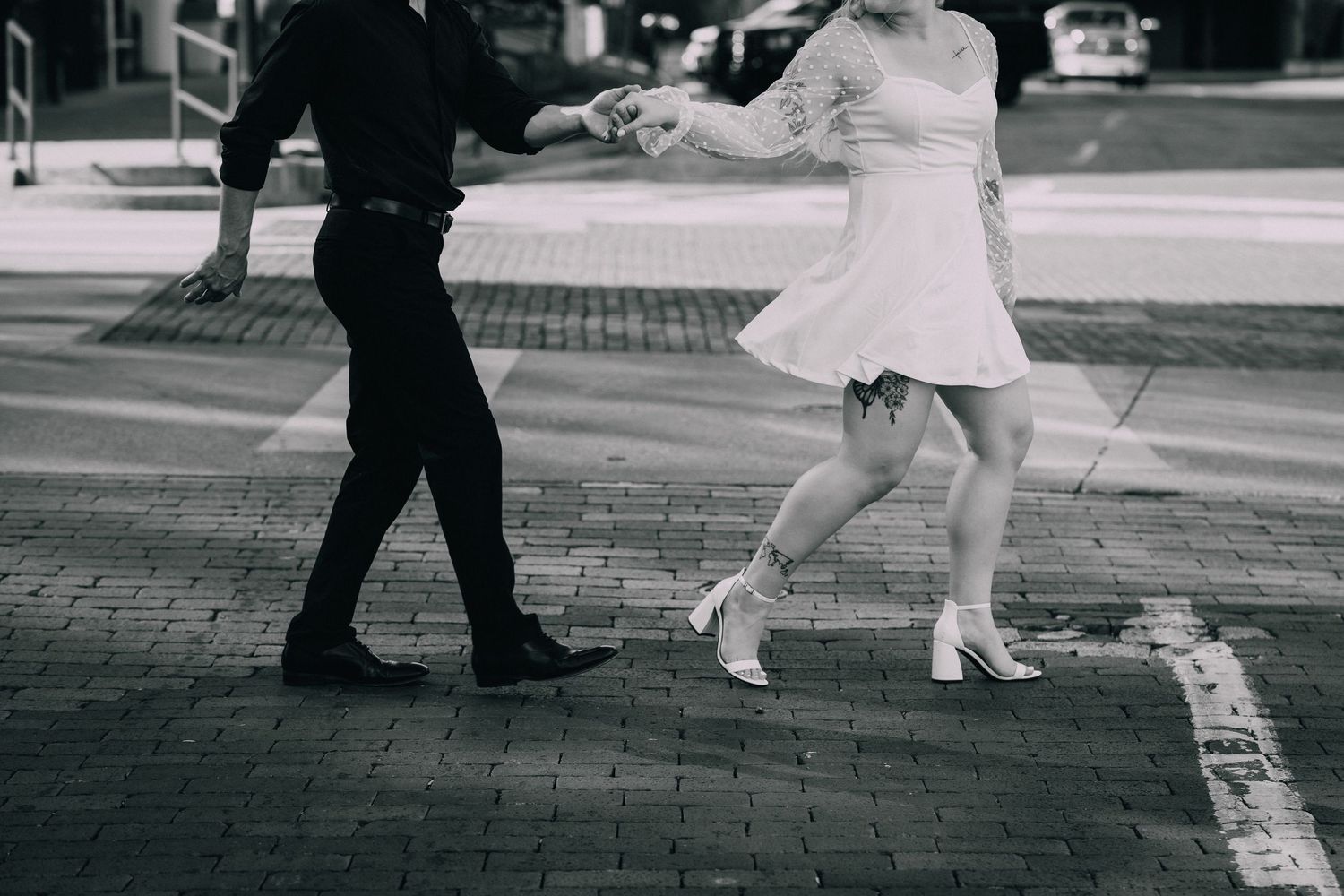 Black and white photo of feet walking on a paved surface during what appears to be a romantic moment.