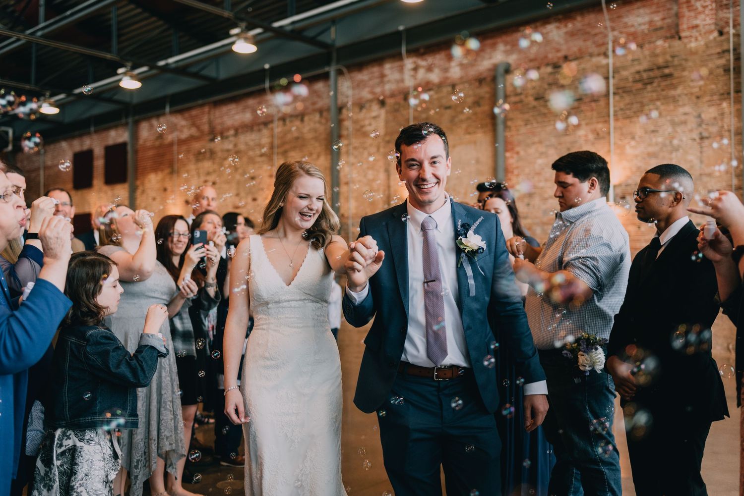 Wedding reception in rustic brick venue with guests celebrating and taking photos.