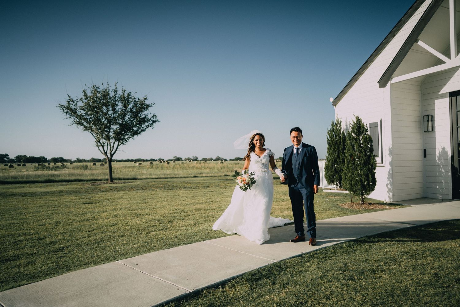 A couple walks along a white pathway outside a modern chapel building.