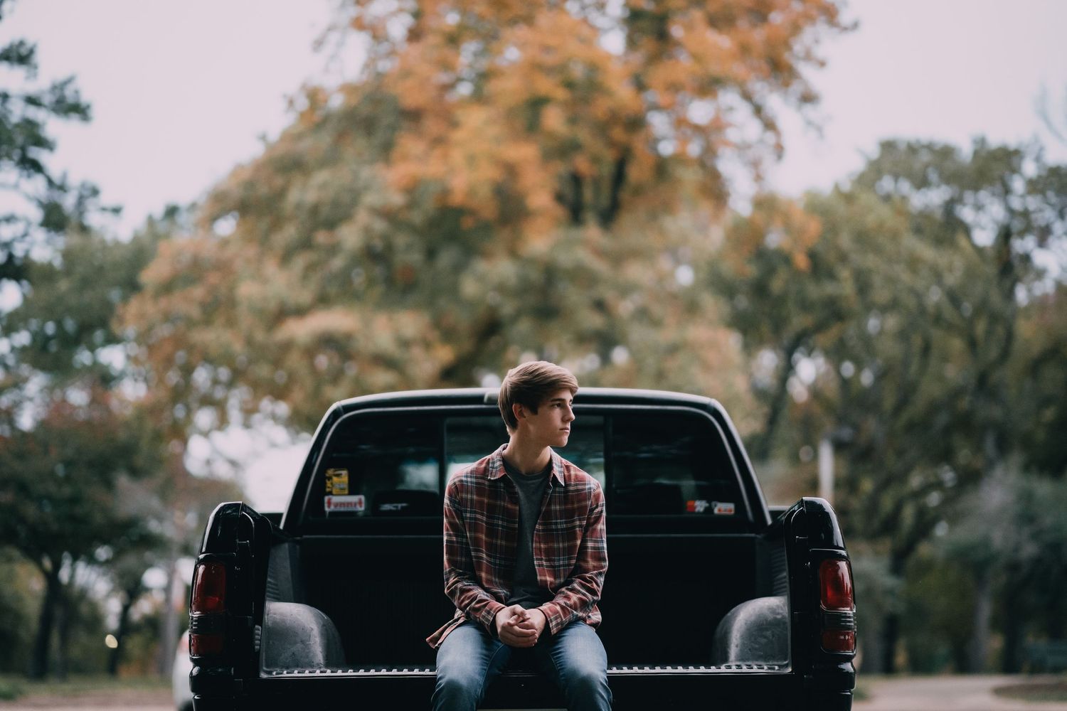 A person sits on the back of a black pickup truck during an outdoor photoshoot.