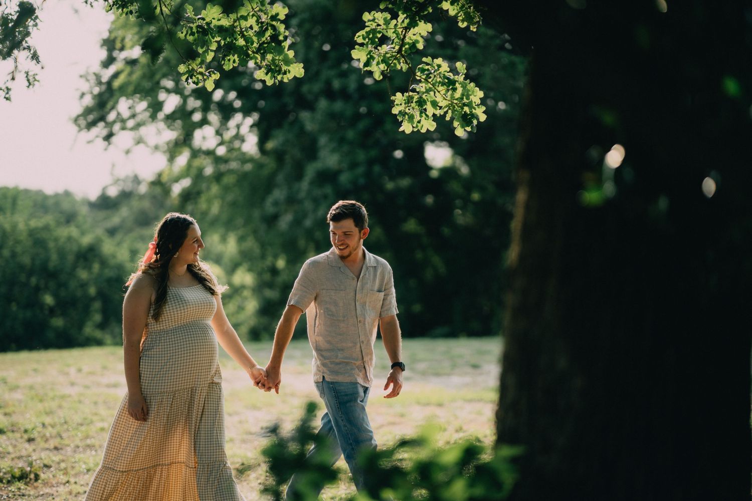A romantic couple holding hands while walking through a sun-dappled forest clearing.