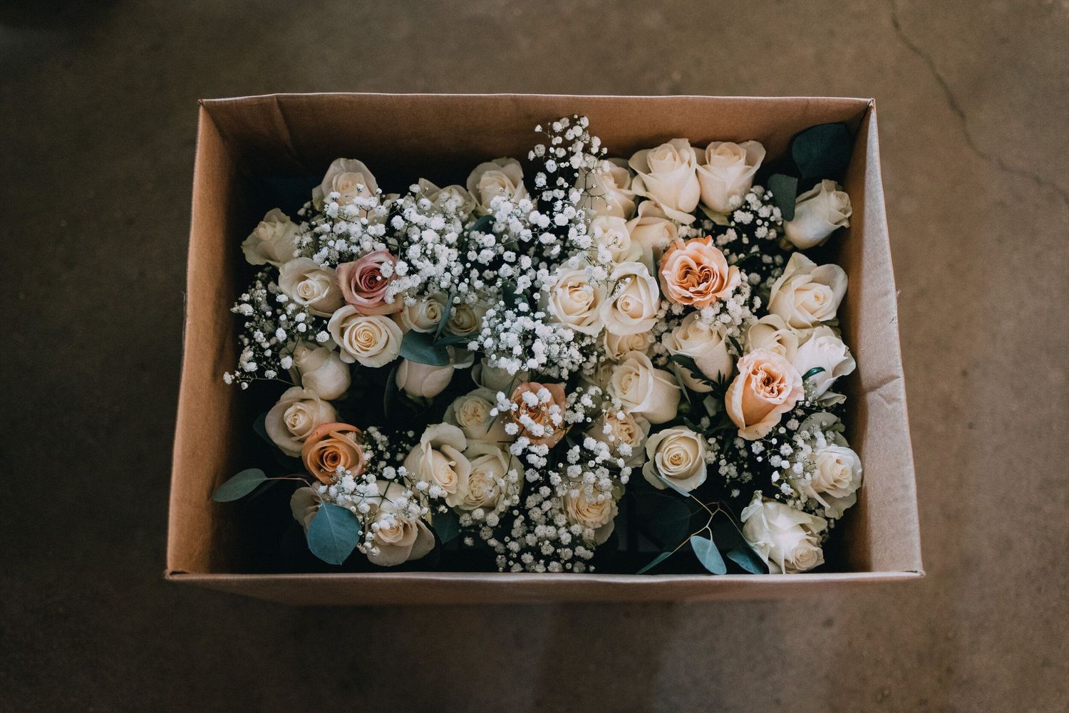 Box filled with delicate white and peach roses and baby's breath flowers.