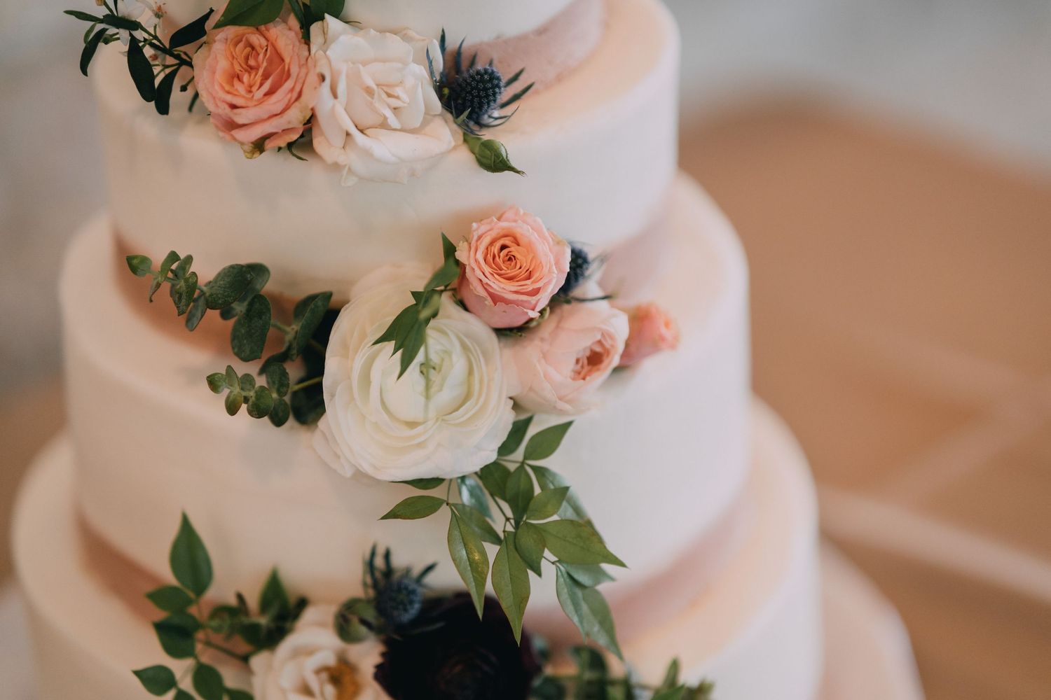 An elegant white wedding cake decorated with peach roses and delicate green foliage.