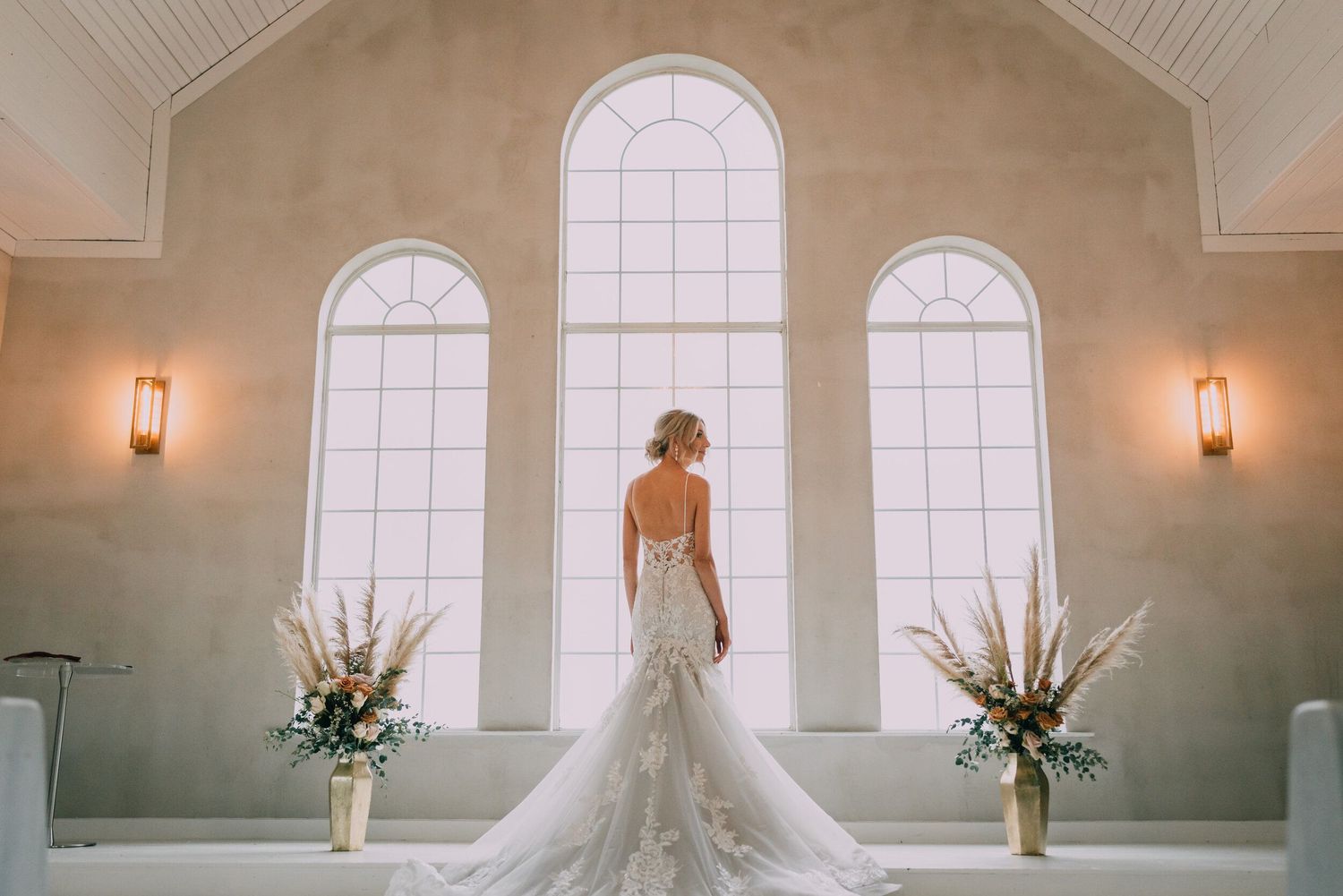 Elegant wedding dress silhouette against arched windows in classic chapel.