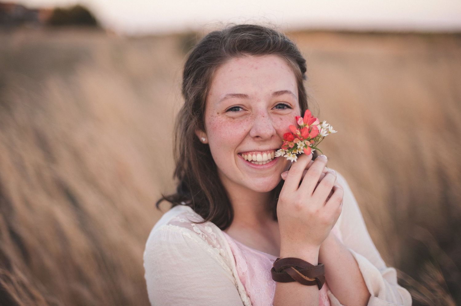 A person holds flowers against a warm sunset backdrop in a natural setting.