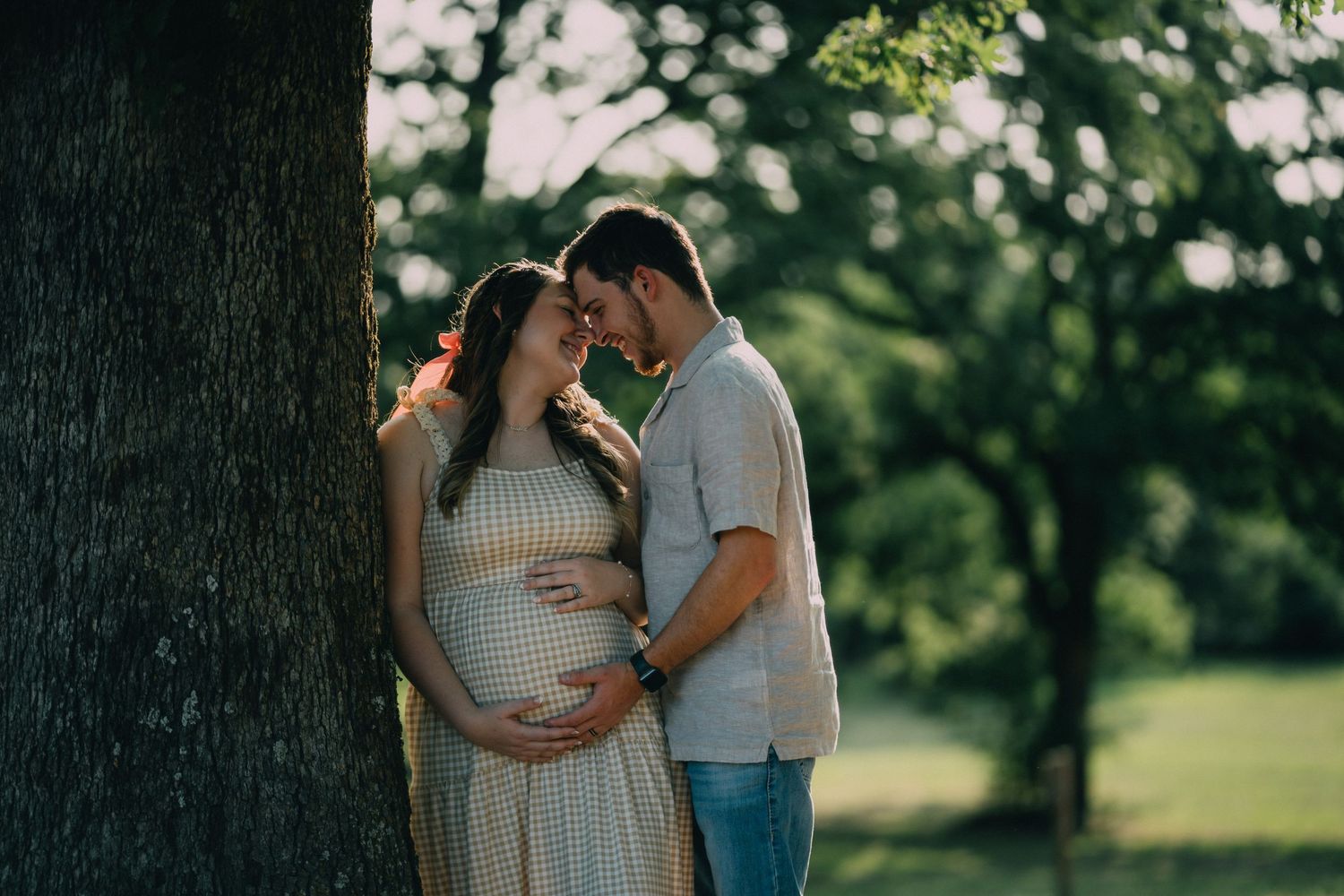 A couple shares an intimate moment under trees during a maternity photoshoot.