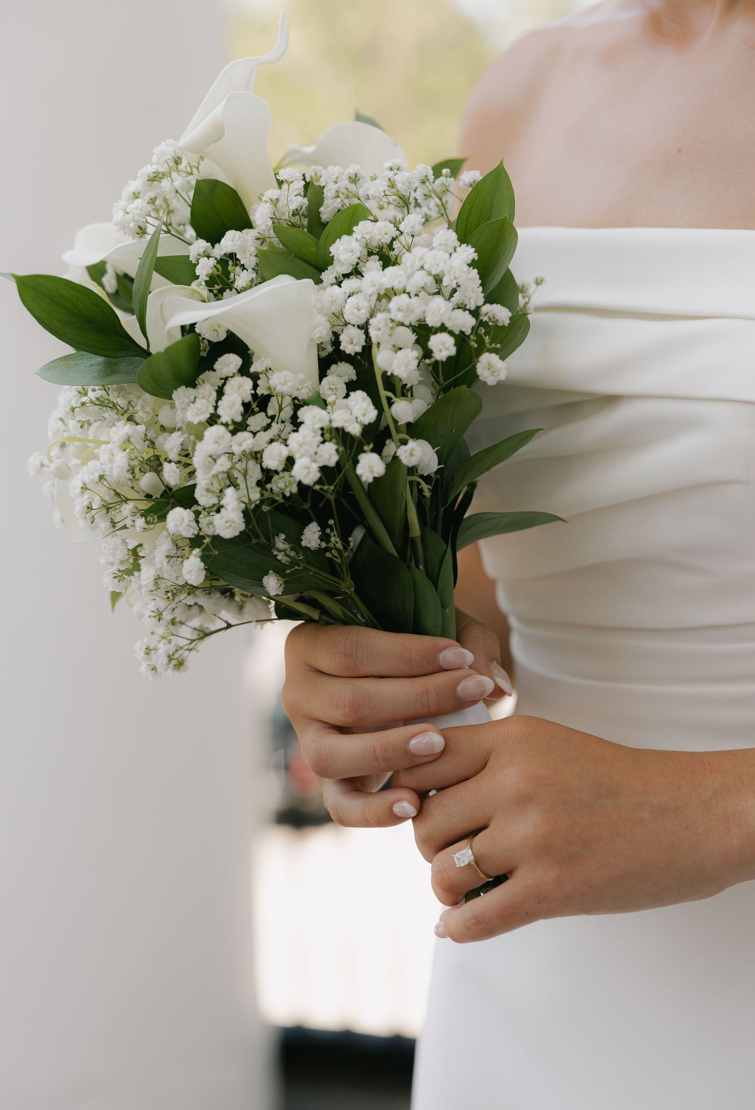 Close-up of bride holding elegant white bouquet with baby's breath and calla lilies.