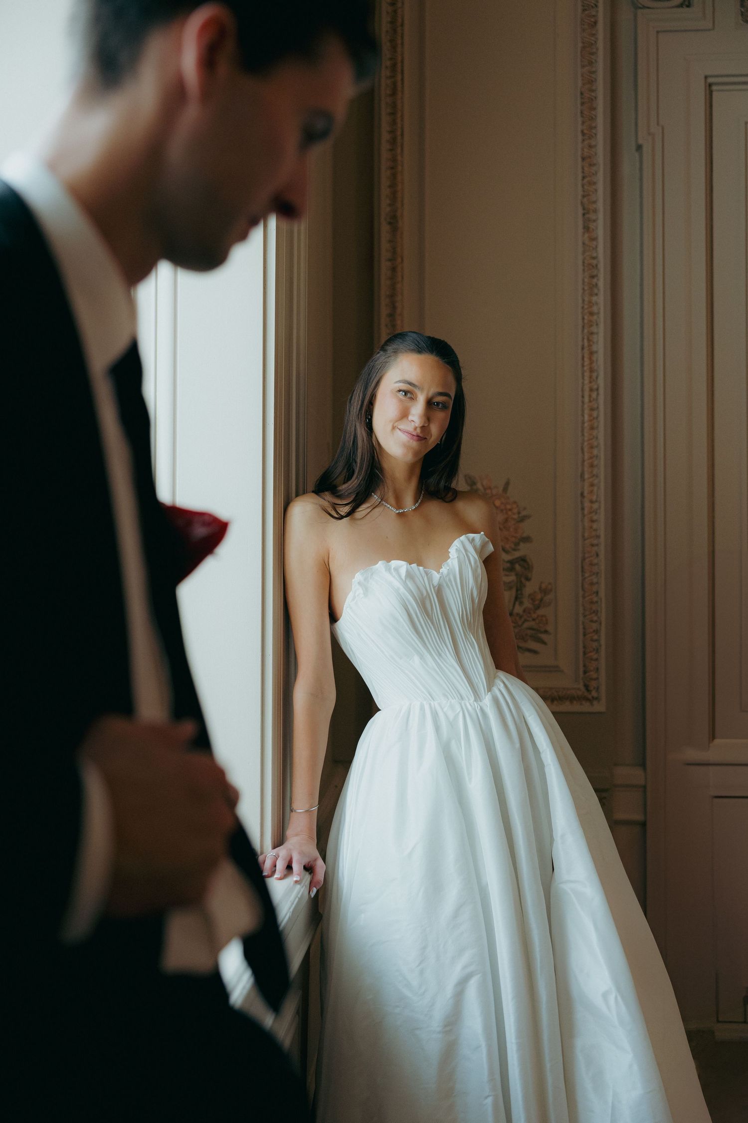 Bride in strapless white ball gown smiling at groom in elegant room during wedding portraits.