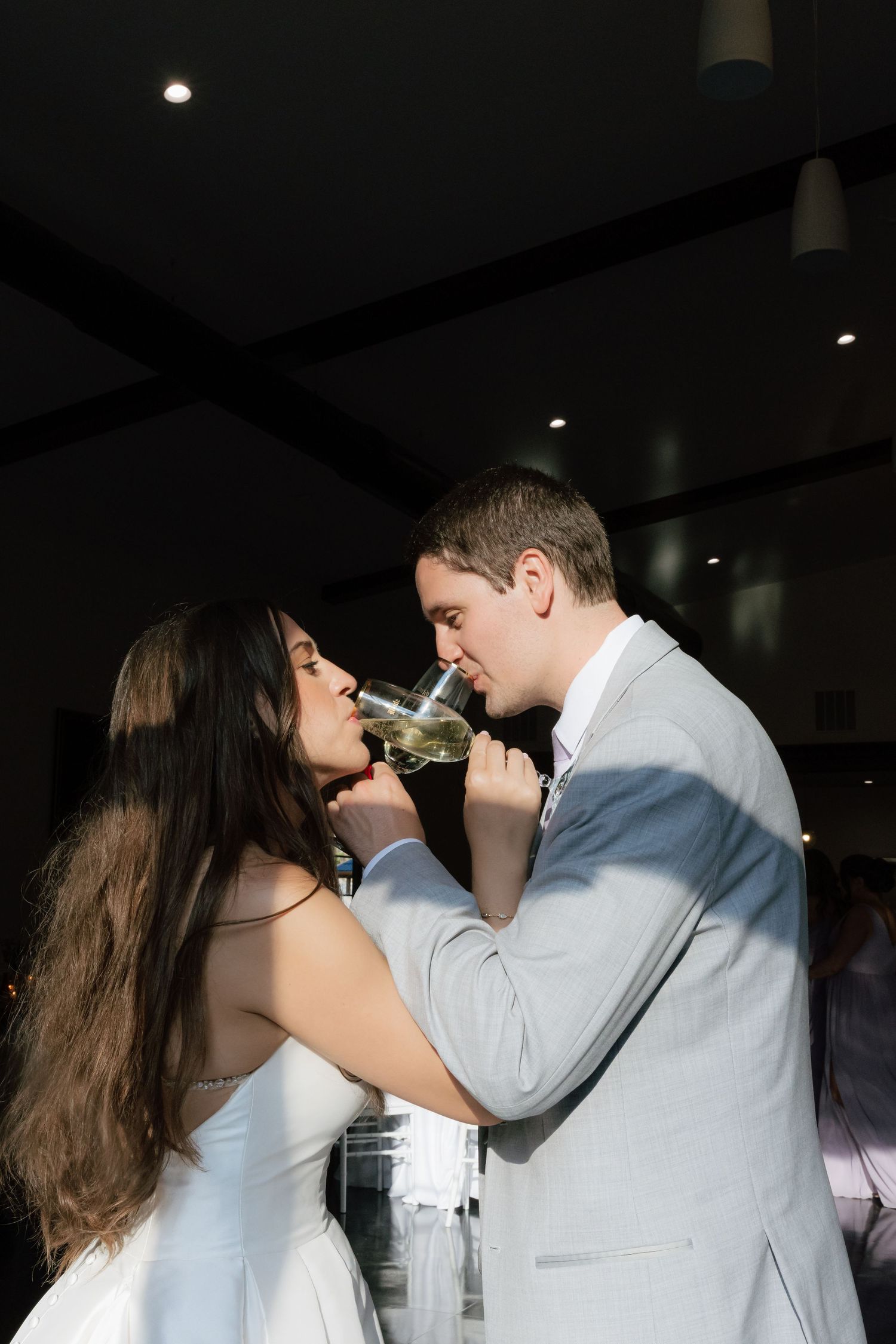 Bride and groom sharing a champagne toast together at their wedding reception, dressed in white gown and gray suit.